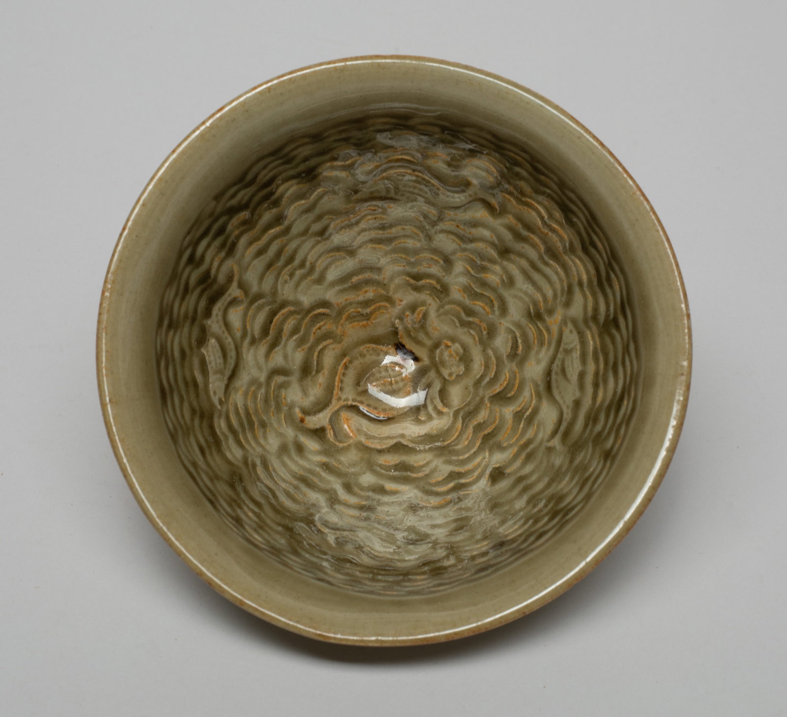 Chinese Yaozhou Ware Porcelain Tea Bowl: The bowl interior walls carved with fish swimming amidst waves, and reversed by recessed hash marks on the exterior walls, the dark olive green glaze applied everywhere except the foot ring. Approx. 4