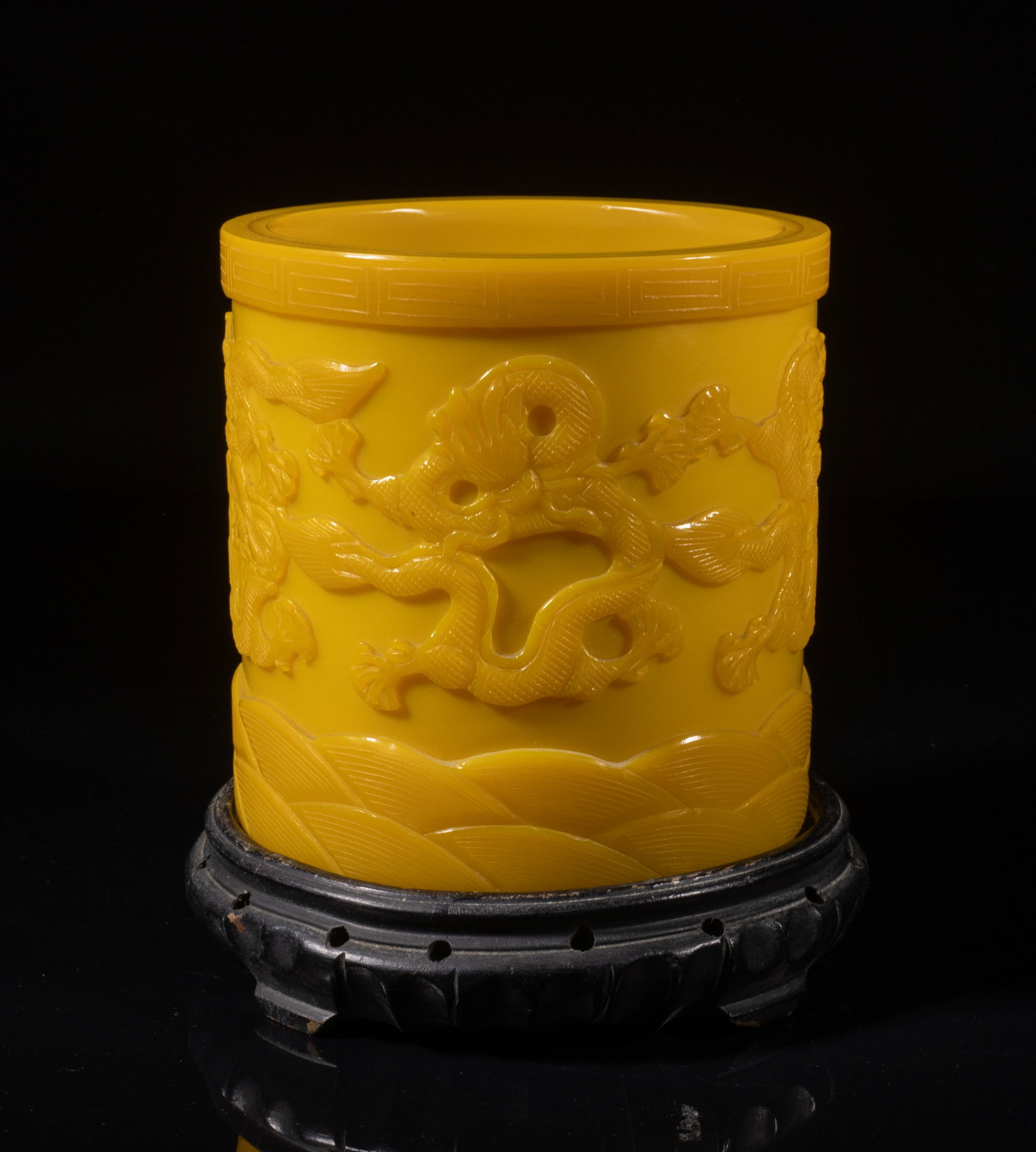 Chinese Royal Yellow Peiking Glass Brush Pot: Chinese opaque royal yellow Peiking glass brush pot of cylindrical form, the exterior carved with sinuous dragons pursuing a ball above waves, the rim with a fret border, with stand. Approx. 6*5.8 inc