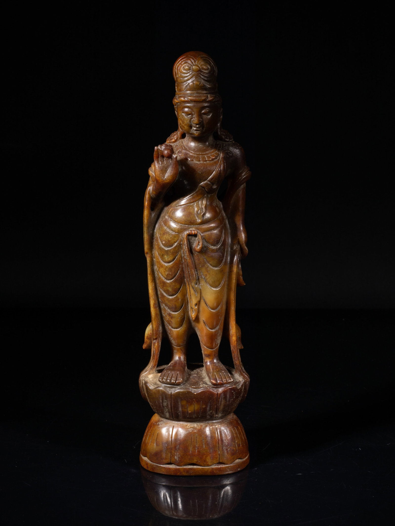 Chinese Stone Carved Sculpture of Buddha: The brown stone Buddha carved standing on a double-layer lotus base, the left hand grasping a long curled scarf and right hand holding a ball, the rounded face with serene expression. Approx. 10.7*2.9