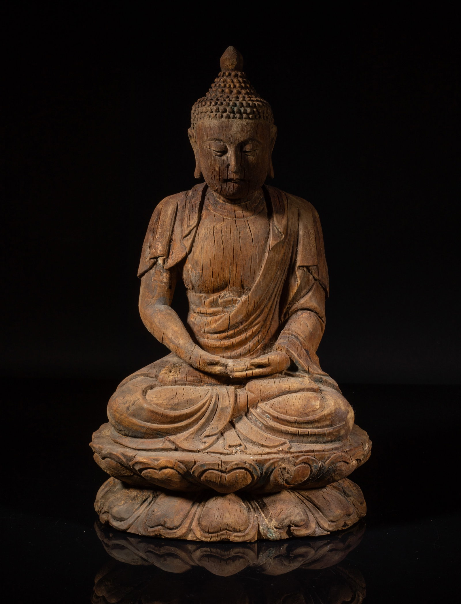 Chinese Wood Sculpture of Buddha: Carved seated in dhyanasana on a double-lotus base, with the hands held in dhyanamudra, wearing a long robe open at the chest, the face with a serene expression and the hair in tight curls covering th