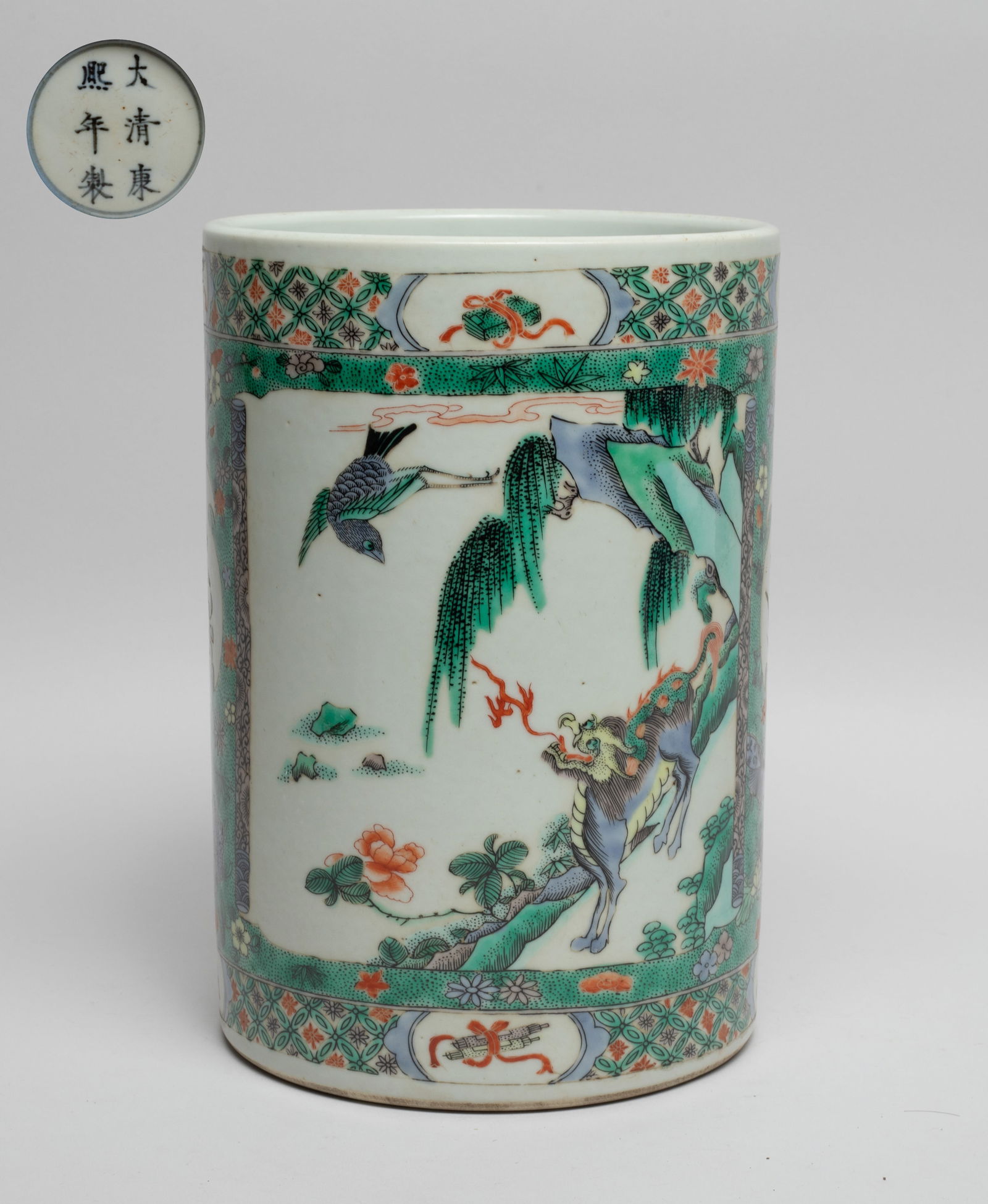 Chinese Wuchai Porcelain Brush Pot: Of cylindrical form, the exterior painted with two rectangular panels of qilin and bird, and two leaf-shaped panels of flowers and butterflies, over green ground suffused with flowers and butterflies,