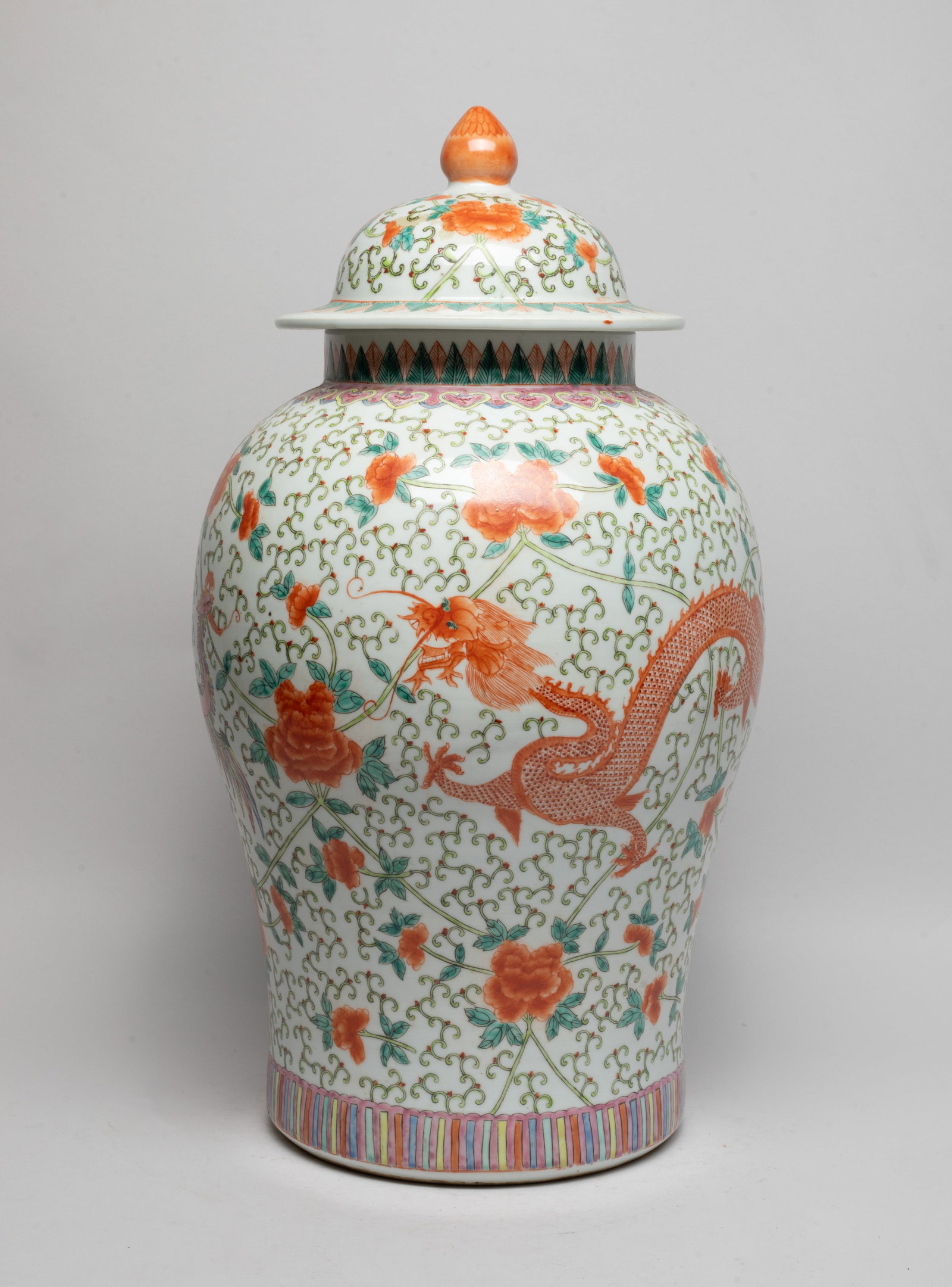 Tall Chinese Famille Rose Porcelain Covered Vase: The vase exterior painted with a phoenix and a copper-red dragon amongst dense meandering floral scrolls, between bands of ruyi heads and lappets, the lid with similar floral scrolls motif. Approx. 19
