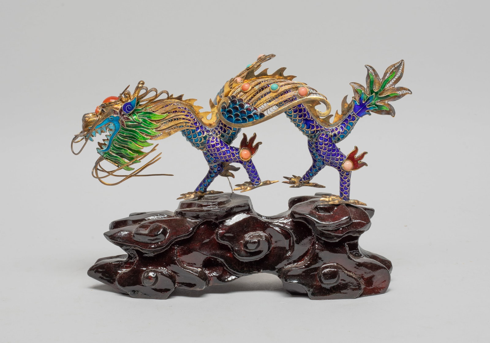 Chinese Gold on Silver Dragon Sculpture: Chinese gold-on-silver reticulated dragon sculpture, with a long sinuous body and a pair of outstretched wings, applied with green and blue glaze, decorated with gemstone, the wood base carved in scro