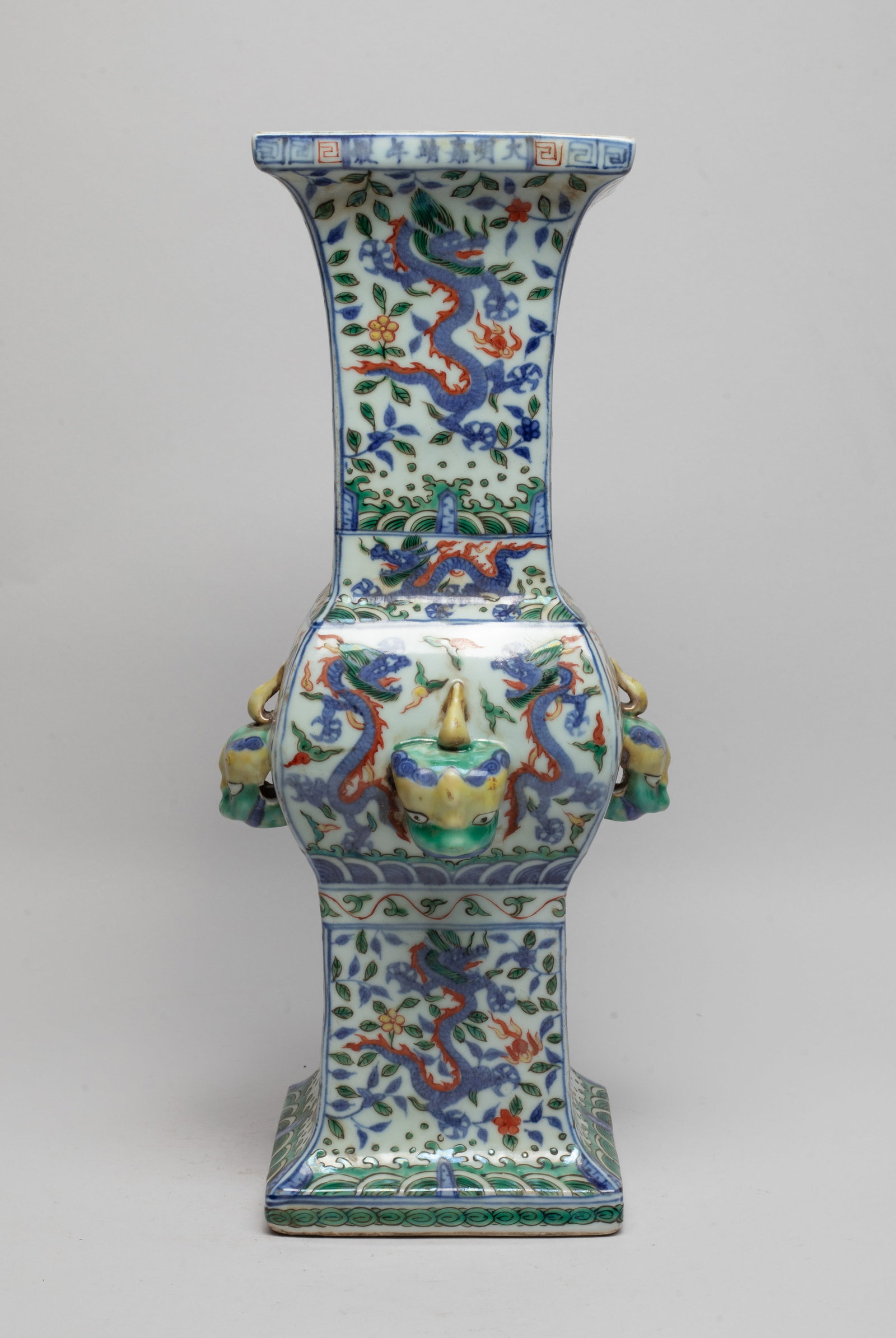 Tall Chinese Wuchai Porcelain Vase: Of archaic gu form, each side at the central bulb painted with pair of dragons above waves and set with a raised beast mask, the upper and lower section painted with dragons amidst flower stems, marke