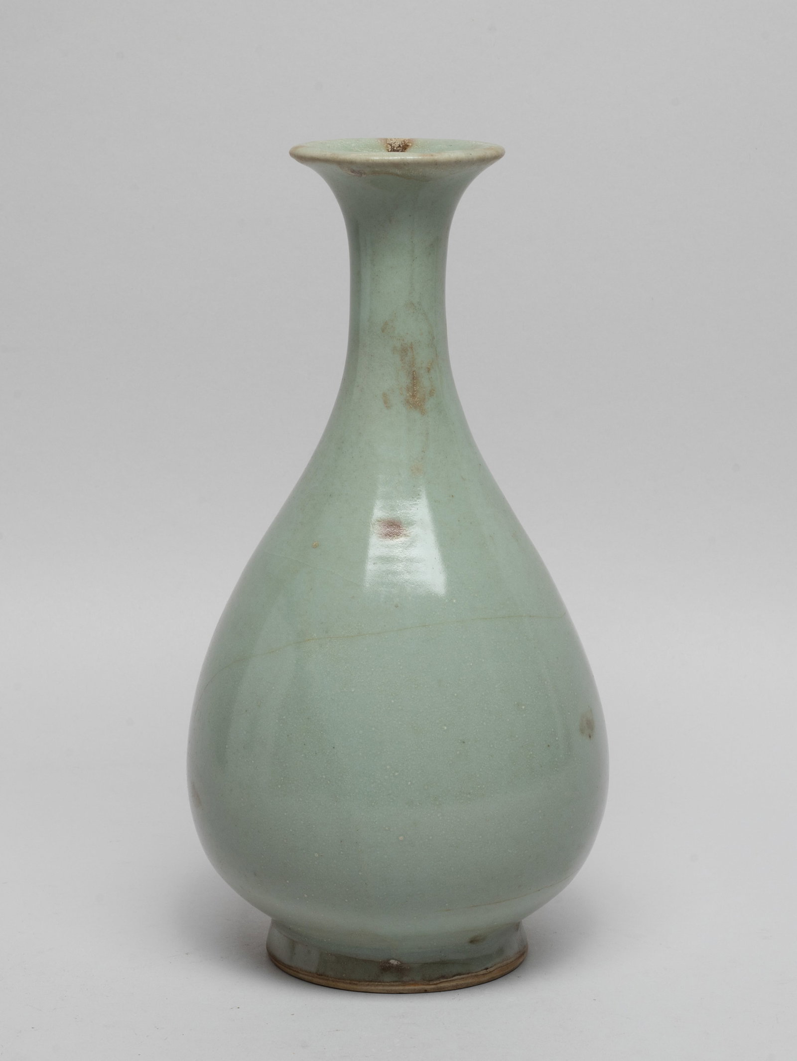 Chinese Longquan Porcelain Vase: The pear-shaped body rising from a splayed foot to a waisted neck and a flared rim, overall covered in soft celadon glaze with brown inclusions and crackles. Approx. 9.2*4.7 inch. The Estate of the Ro