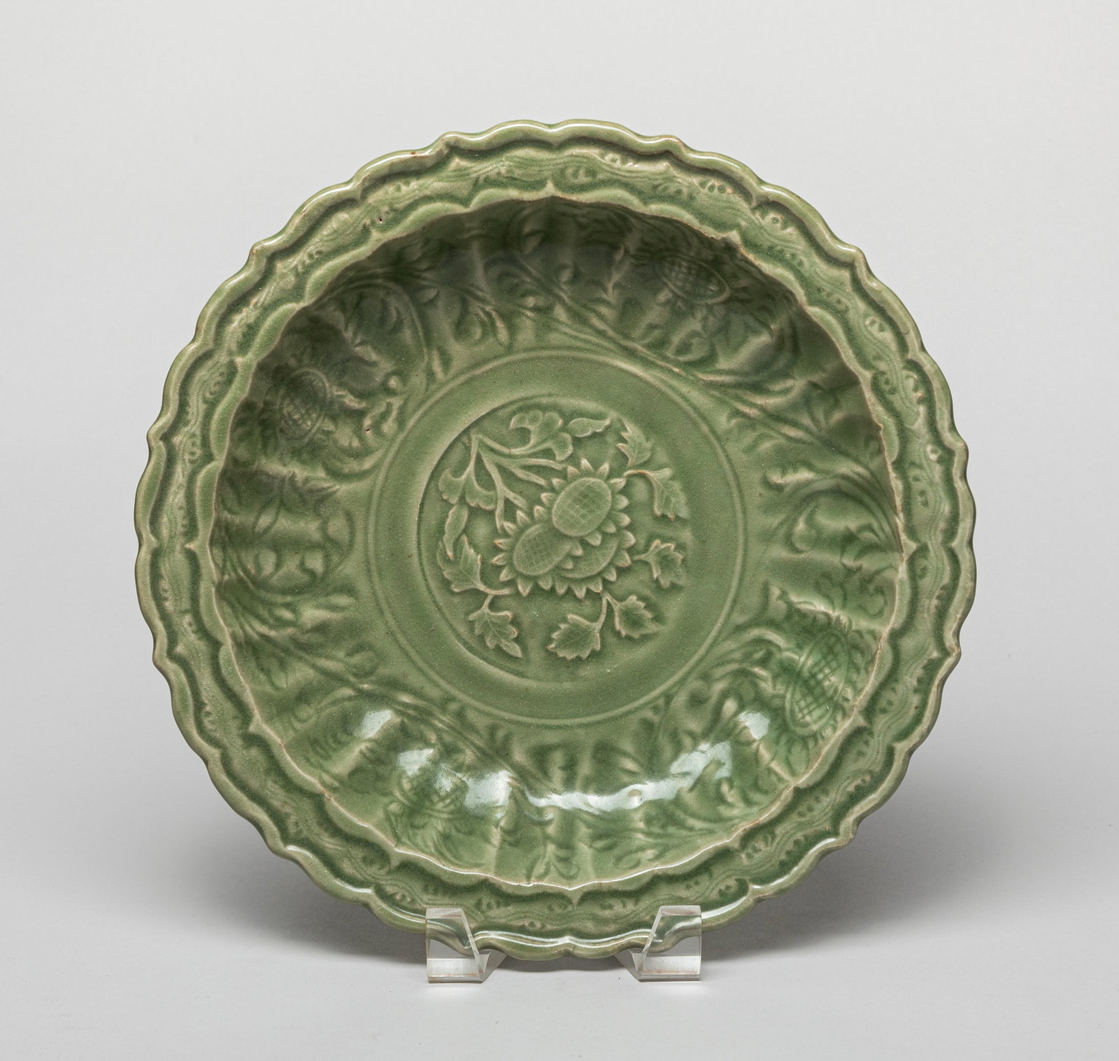 Chinese Longquan Porcelain Charger: Potted with a scalloped rim and conforming ribbed cavetto, carved with peony sprays that surround central flowers, the rich celadon glaze covering all surfaces. Approx. 10.8*2.4 inch.