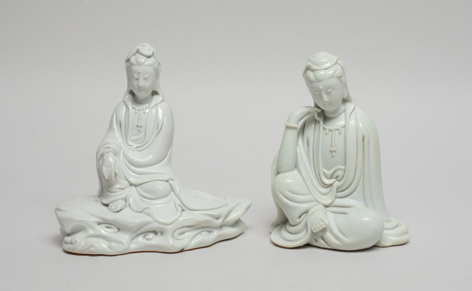 Two Chinese Blanc De Porcelain Sculptures: Two Chinese porcelain seated Kuanyin sculptures, each wearing a loose-fitting robe open at the chest revealing a bead necklace, the exterior applied in even white glaze. Approx. 5*5*2.7 inch (larger).