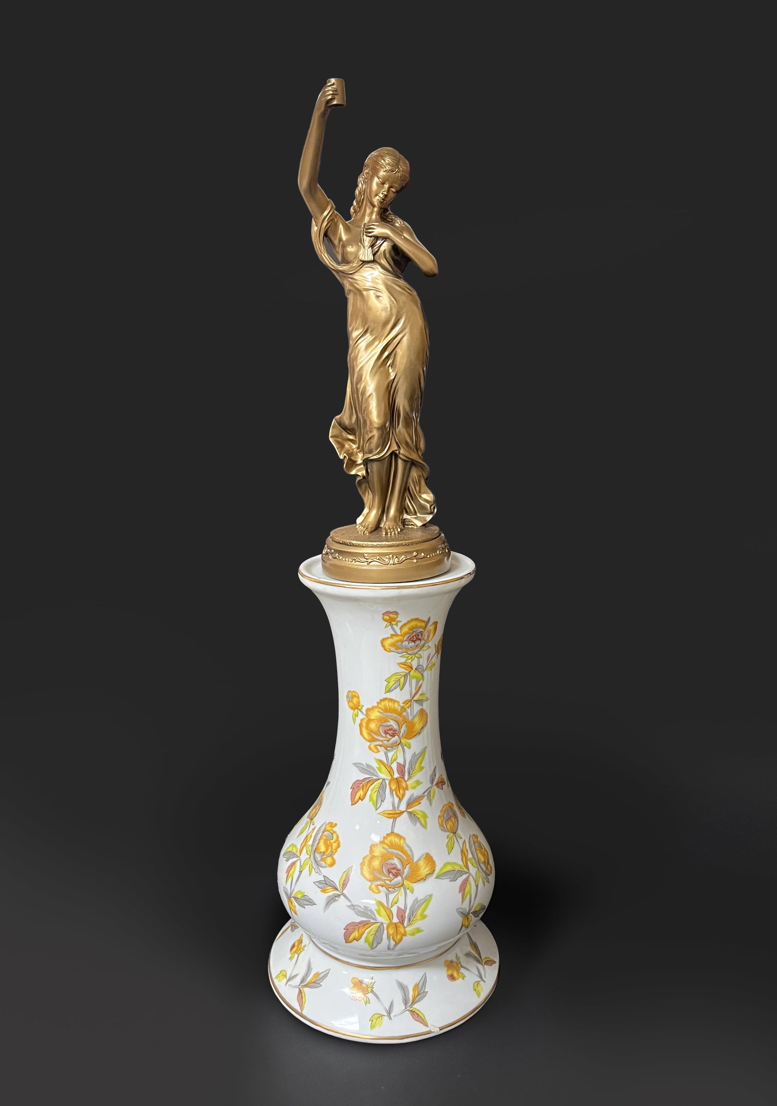 Gold Color Sculpture on Porcelain: The sculpture moulded as a standing woman holding a bird in her left hand and a cup in right hand, with a circular base, the tall vase form porcelain stand decorated with yellow blossoming flowers. Ap