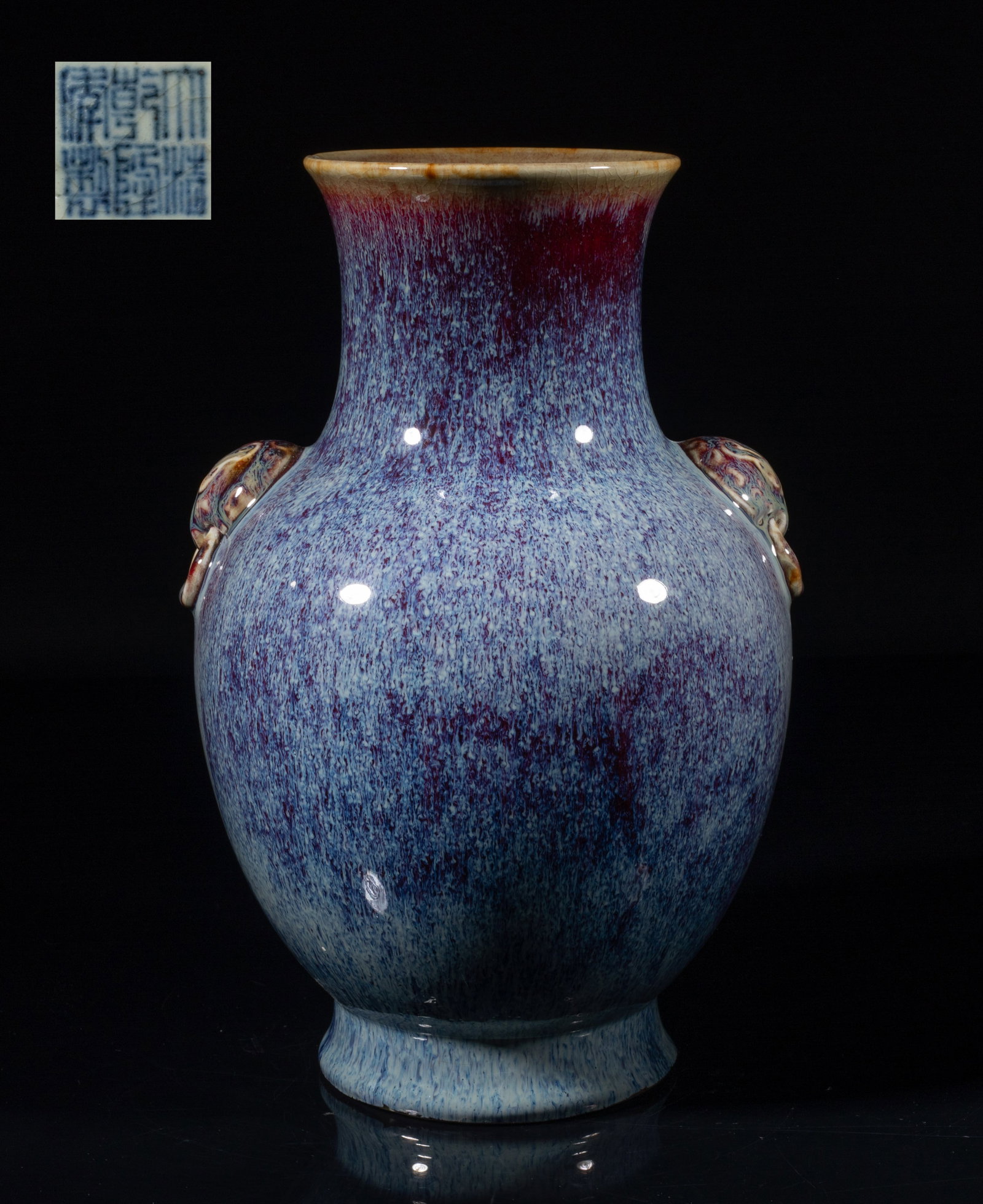 Tall Chinese Flambe Glazed Porcelain Vase: The ovoid body rising from a splayed foot to a waisted neck, flanked by a pair of raised faux-ring mask handles, the exterior and interior neck covered in dark purple-red glaze suffused with milky-blu