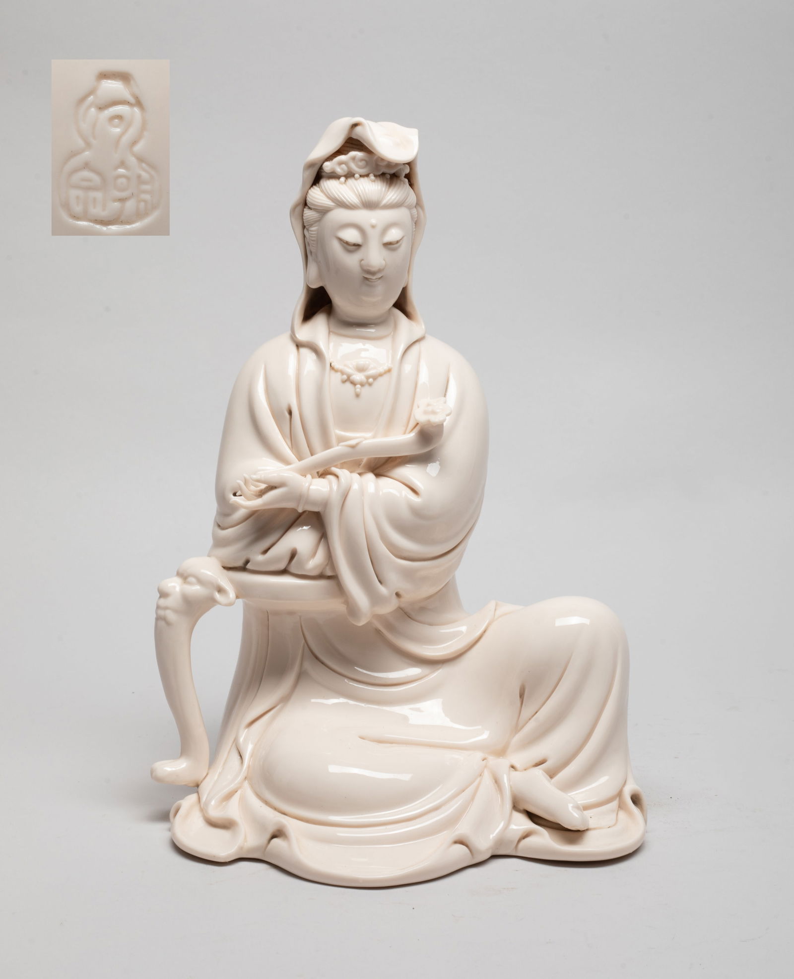 Chinese Export Blanc De Porcelain Kuanyin: The seated Kuanyin wearing a long flowing robe, the left hand holding a ruyi and right arm resting on a beast form stand, the face with serene expression, applied in creamy glaze. Approx. 11*7.5*6 inc