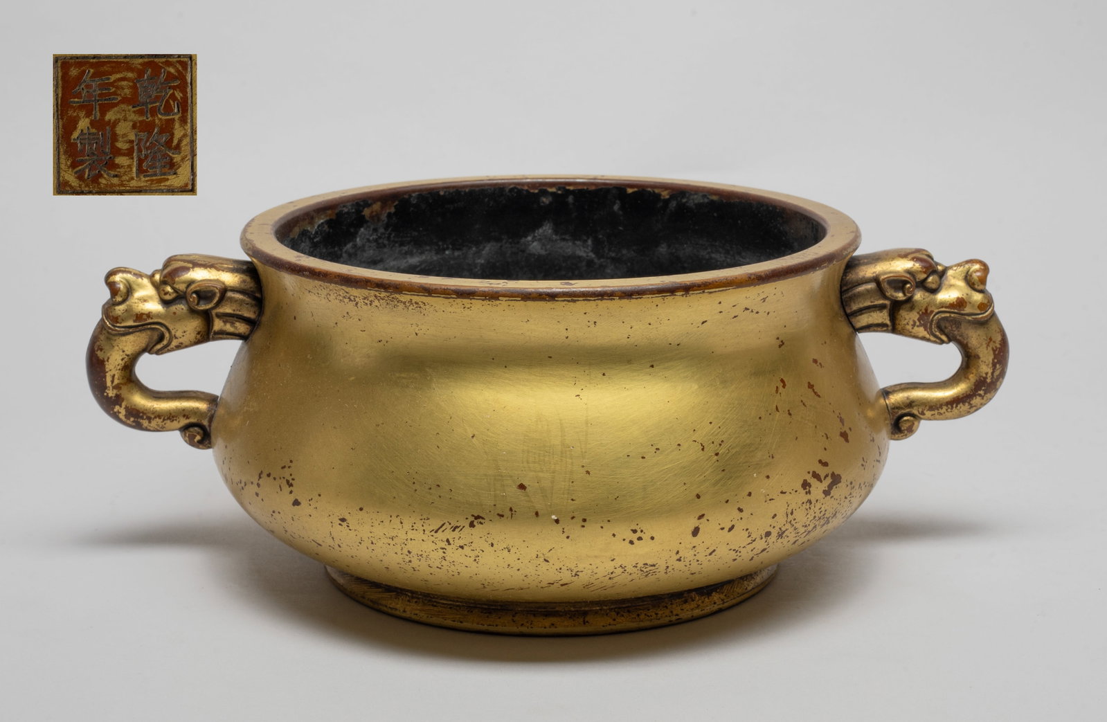 Large Chinese Gilt Bronze Censer: Of compressed form rising from a short splayed foot to a broad waisted neck, flanked by a pair of handles issuing from beast heads, the bottom incised with a four-character mark. Approx. 10.5*7.5*4 in