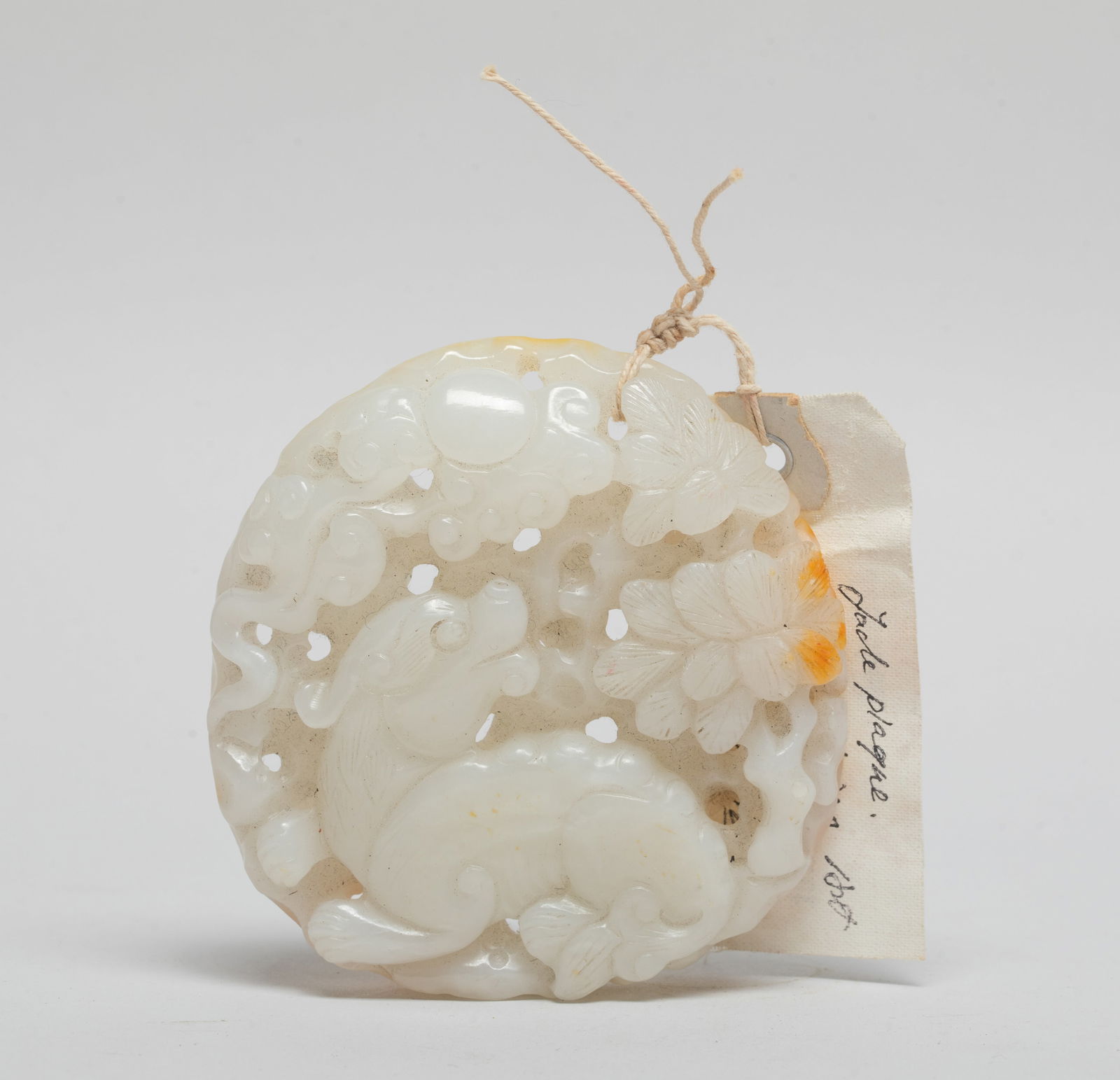 Estate Chinese Russet Jade Pendant: The rounded pendant carved and reticulated with a beast recumbent beneath sun and clouds, its head turned backwards gazing at a pine tree, the stone of white color with russet inclusions. Approx. 3.13