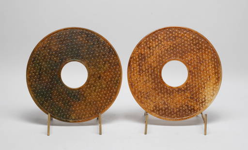 Two Large Chinese Jade Like Bi: Two large Chinese jade-like bi with stands, each of circular shape drilled with an aperture at the centre, carved with raised spirals on both sides, the stone of mottled russet tone. Approx. 7.8 inch