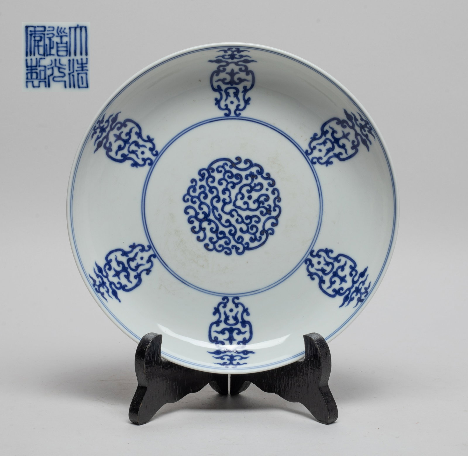 Chinese Blue & White Porcelain Plate w/ Stand: The plate interior decorated with stylized scrolls, the exterior with a band of ruyi scrolls, the bottom inscribed with a six-character mark, with stand. Approx. 7.4 inch D (w/o stand).