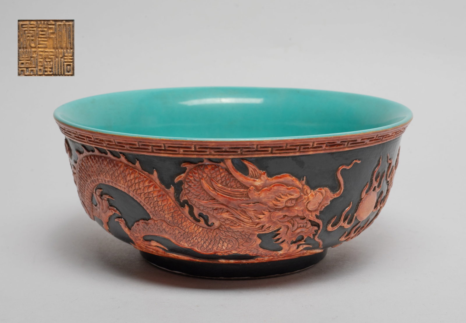 Chinese Export Modeled Porcelain Bowl: The bowl exterior carved and painted in copper-red with a pair of dragons pursuing a flaming pearl amidst clouds above waves, against black glazed background, the interior and bottom turquoise glazed,