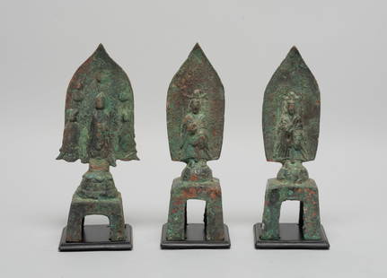 Set Chinese Bronze Sculptures of Buddha: Set of three bronze sculptures, each cast with Buddha standing in front of petal-shaped flame on pedestal, the hands in abhaya mudra, wherein one Buddha flanked by attendant Buddha, with wood bases. A