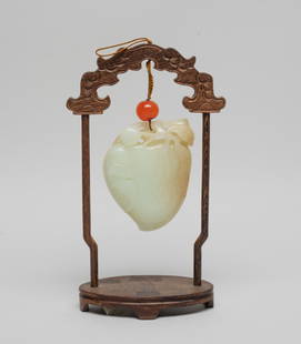 Estate Chinese Export Jade Plaque: Naturalistically carved as a large flattened peach borne on a leafy stem issuing smaller peaches, with a bat on either side, the stone of white tone with russet inclusions, with an agate bead suspende