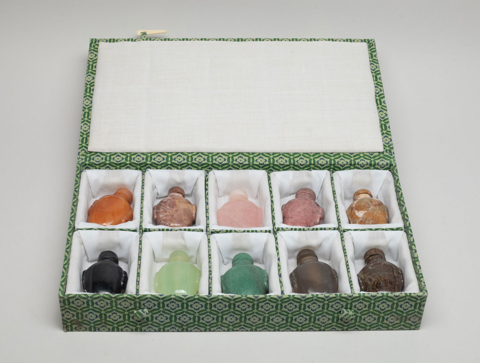 Estate Chinese Jade, Stone Carved Snuff Bottles: Set of ten Chinese jade, stone and quartz carved snuff bottles, each of flattened ovoid form carved with a pair of faux-ring masks and set with a matched stopper, with box. Approx. 2.4*1.7*1.1 inch (r