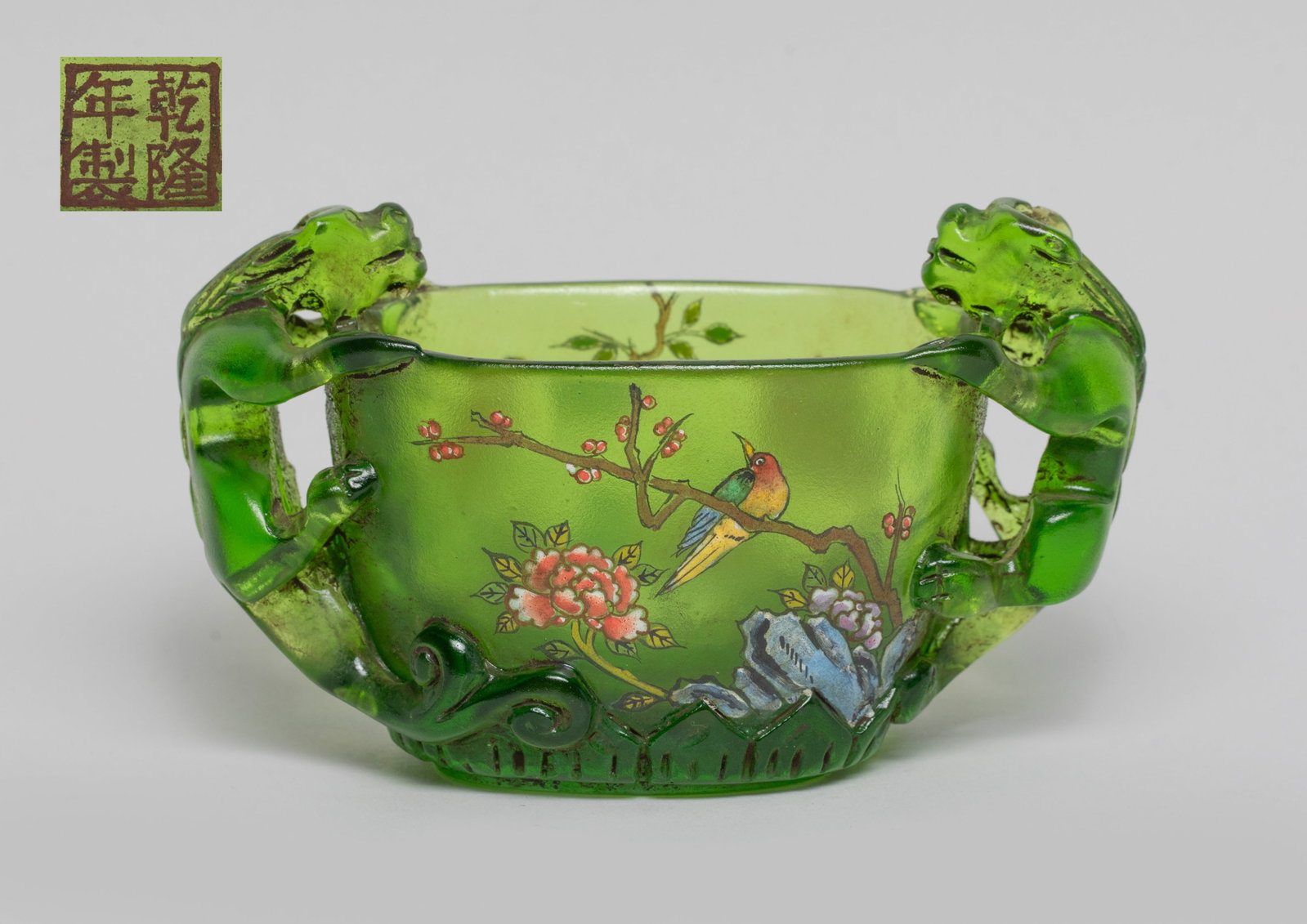 Chinese Enameled Peiking Glass Water Pot: The water pot exterior enameled and painted with bird, flowers and rockery on translucent green glass body, flanked by a pair of clambering chilong forming handles, the bottom with a seal mark. Approx