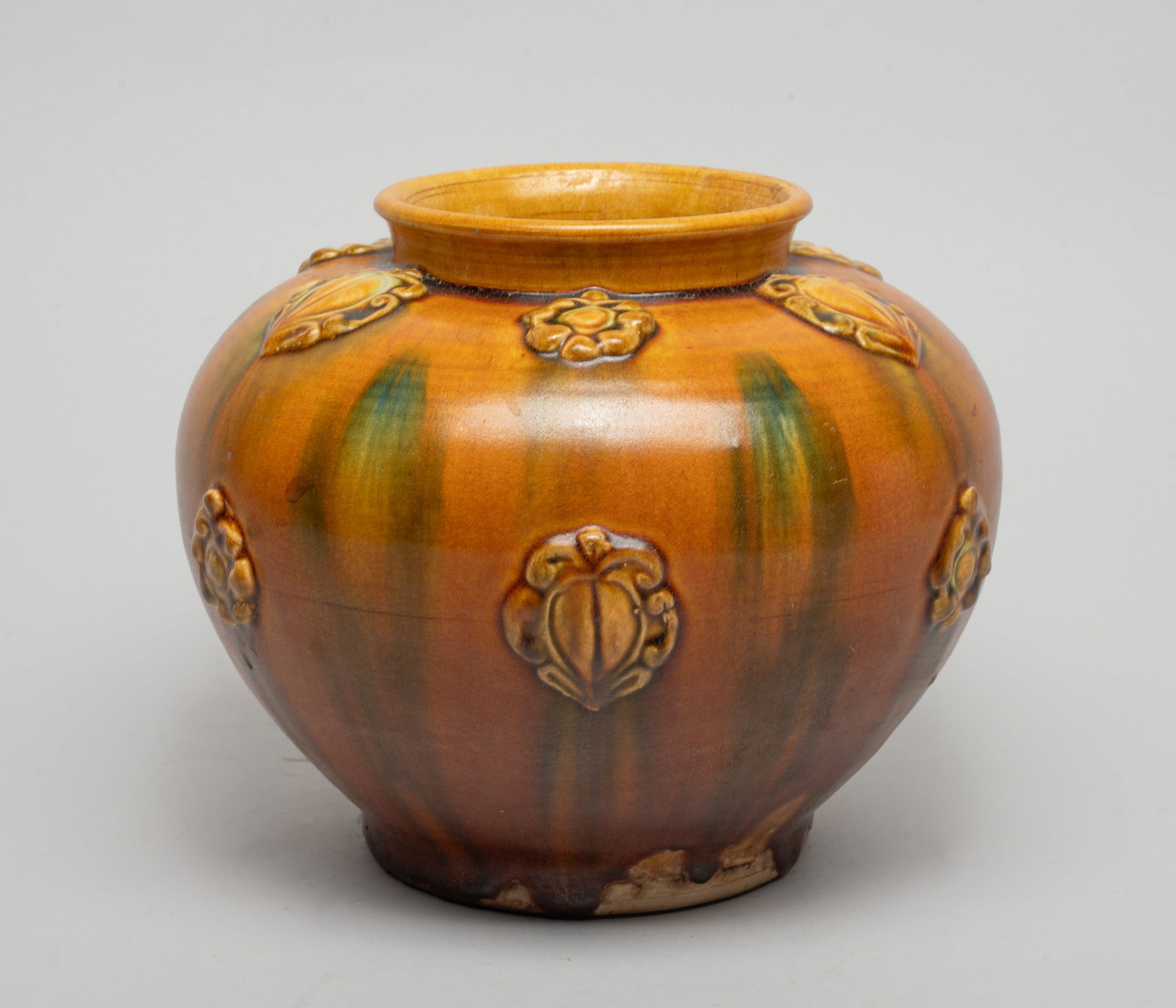 Chinese Sanchai Stoneware Jar: Of tapered ovoid form, the exterior carved in raised relief with stylized flowers and leaves, the exterior applied with beige, brown and green glaze. Approx. 6.4*7.5 inch.
