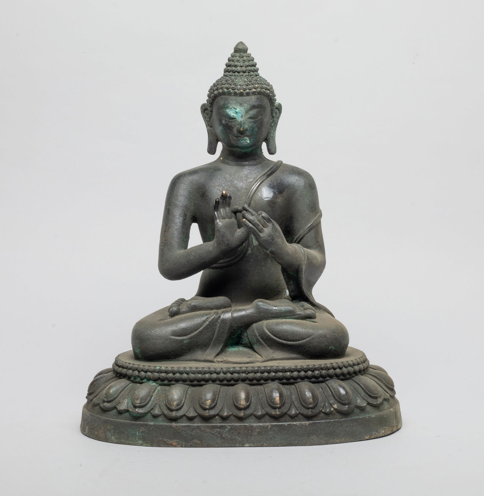 Large Chinese Bronze Sculpture of Buddha: His wide face framed by curls rising up to a domed finial on his ushnisha, flanked by a pair of pendulous ears, sits dhyanasana on a lotus plinth with his hands in dharmachakra mudra. Approx. 12.7*10.