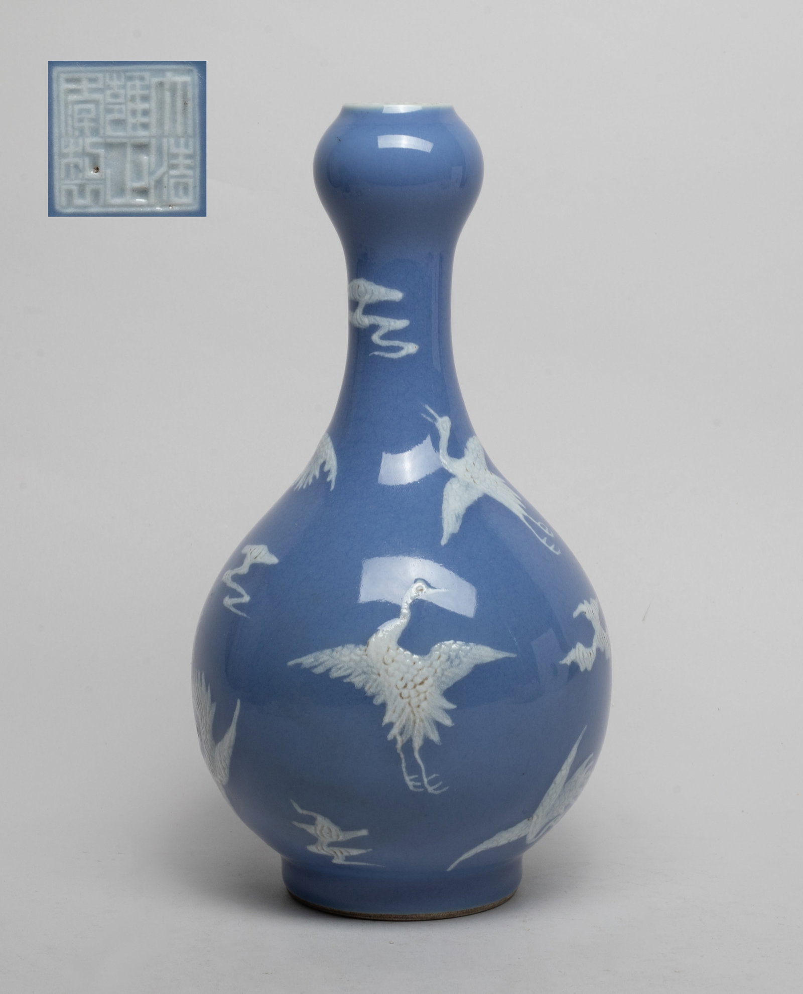 Chinese Export Porcelain Cabinet Vase: The globular body rising from a short foot to a slender neck with a garlic mouth, the exterior decorated with cranes flying amidst scrolling clouds in white color on lavender-blue glazed background, t