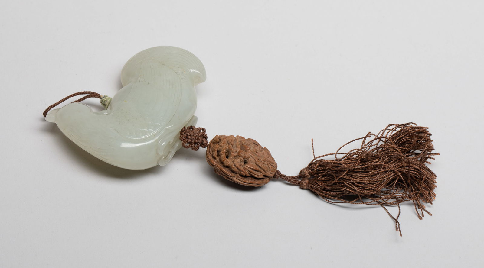 Rare Chinese White Jade, Carved Nut Pendant: Depicting a bird with its head turned backwards, the bird's body flanked by finely picked out plumage, the jade of white colour, the nut pendant carved in openwork with Luohan and pine trees. Approx.