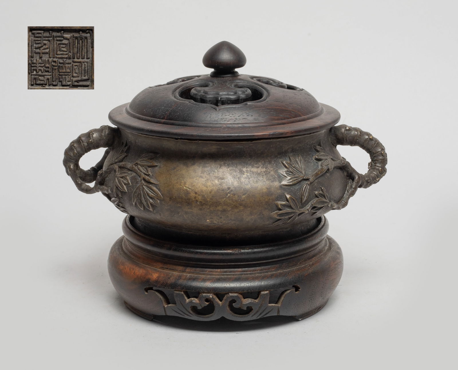 Estate Chinese Bronze Censer w/ Cover: Of compressed form with a splayed foot and a short waisted neck, the handles cast in bamboo form issuing bamboo leaves, the bottom inscribed with a six-character mask, with a wood lid and a wood stand