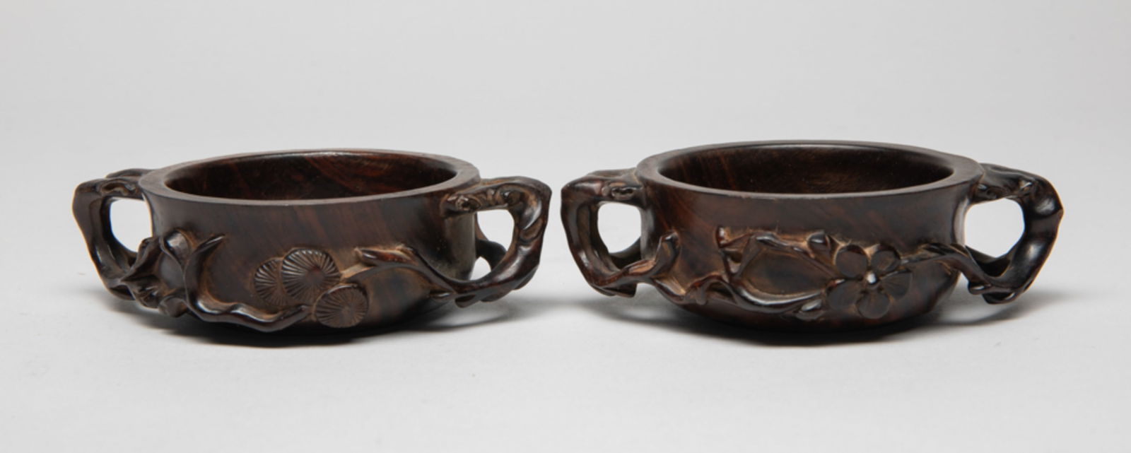 Two Chinese Wood Libation Cups: Each cup of shallow rounded form, carved with gnarled branches issuing blossoms and pine needles forming the handles. Approx. 4.1*2.9*1.1 inch (each).