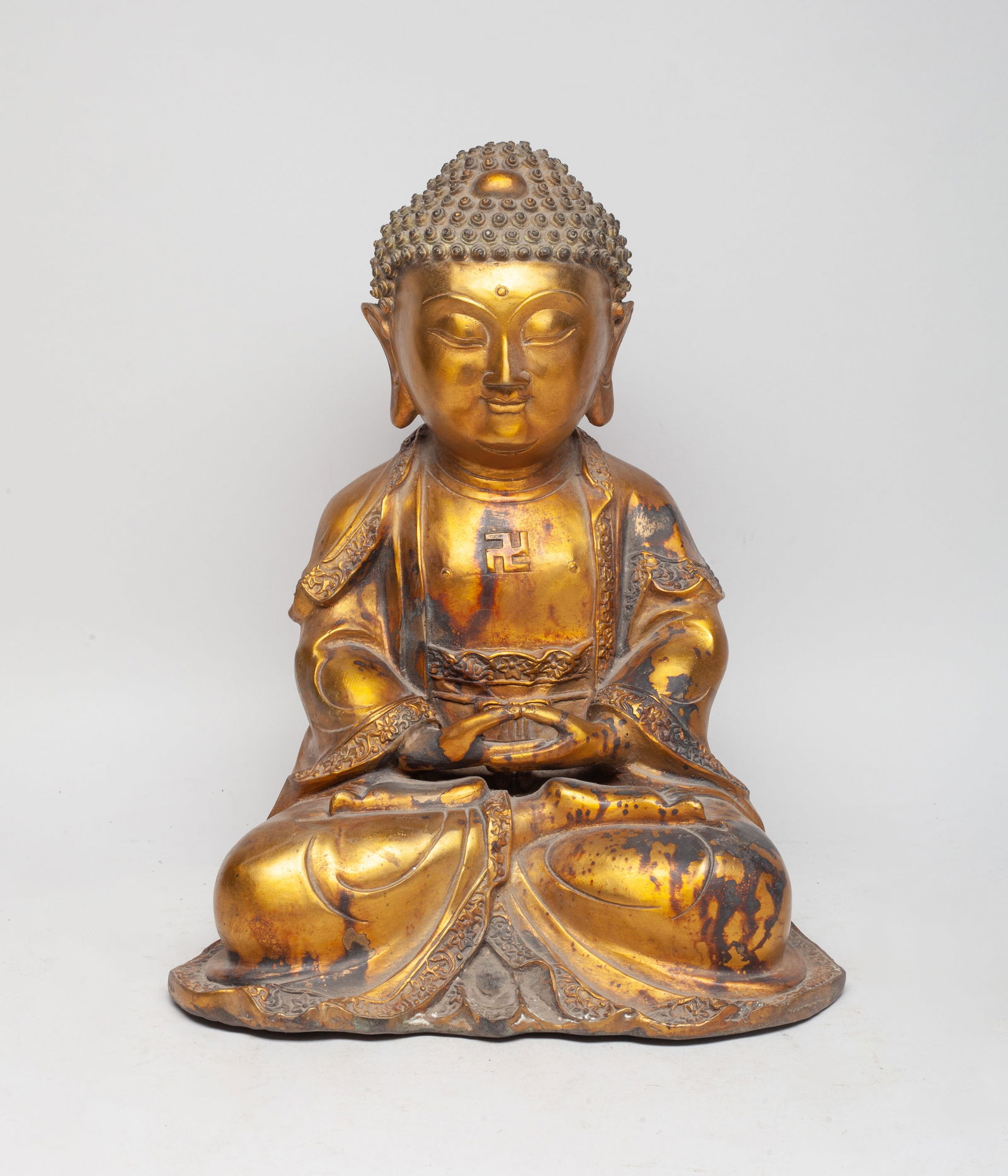 Large Chinese Temple Used Gilt Bronze Buddha: With tight hair curls, full face, and pendulous earlobes, attired in the loose garments of a monk as he sits dhyanasana, open at the chest revealing a swastika symbol. Approx. 11.6*9.5*6.2 inch.