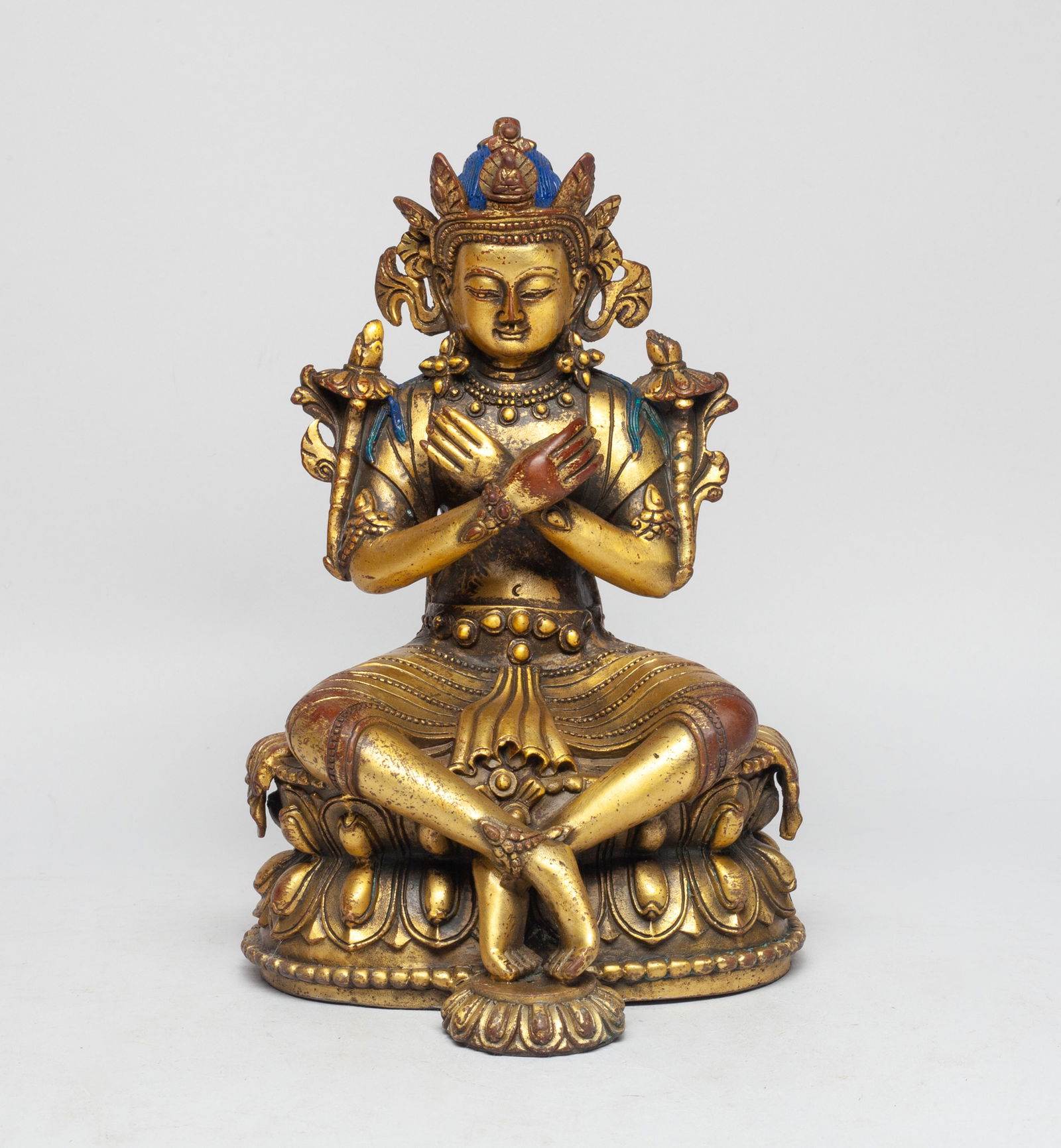 Chinese Sino-Tibetan Gilt Bronze Buddha: The Buddha cast sitting on a double lotus plinth, the hands in an unknown sacred mudra, his arms and torso displaying elaborate jewelry and blossoming flowers, his head enveloped in a five-lobed crown
