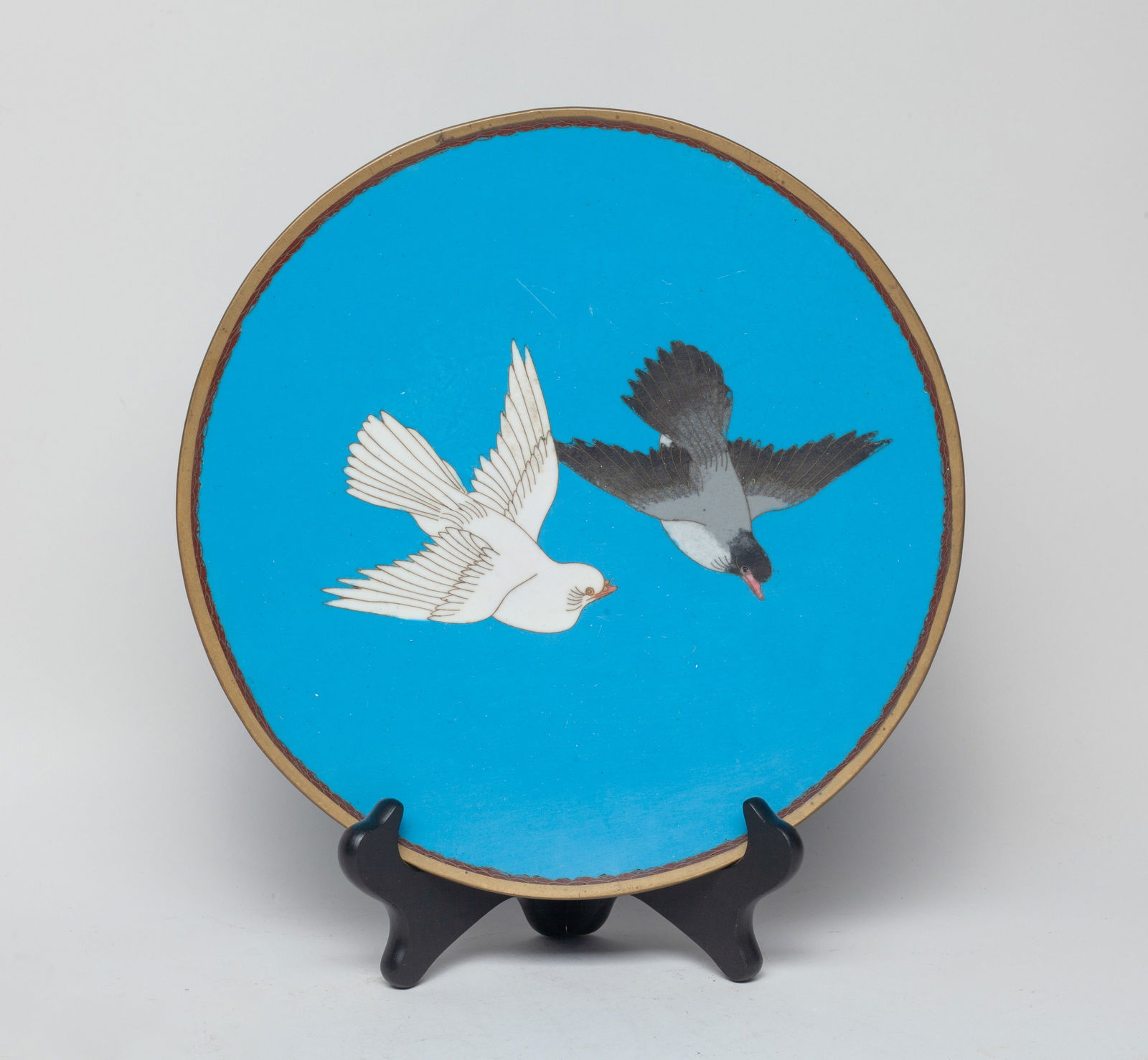 Japanese Antique Meiji Cloisonne Plate: The circular plate interior enameled and painted with a pair of flying birds, against blue glazed background, the underside decorated with scrolls, with stand. Approx. 9.6 inch D (w/o stand).