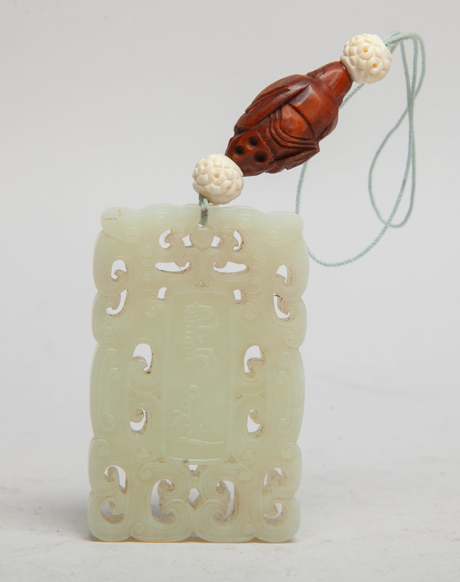Rare Chinese Cream White Jade Pendant: Of rectangular shape, carved in openwork with a pair of stylized dragons encircling a central panel of two characters, with a seed carved Buddha form bead, and two bone beads carved flowers. Approx. 2