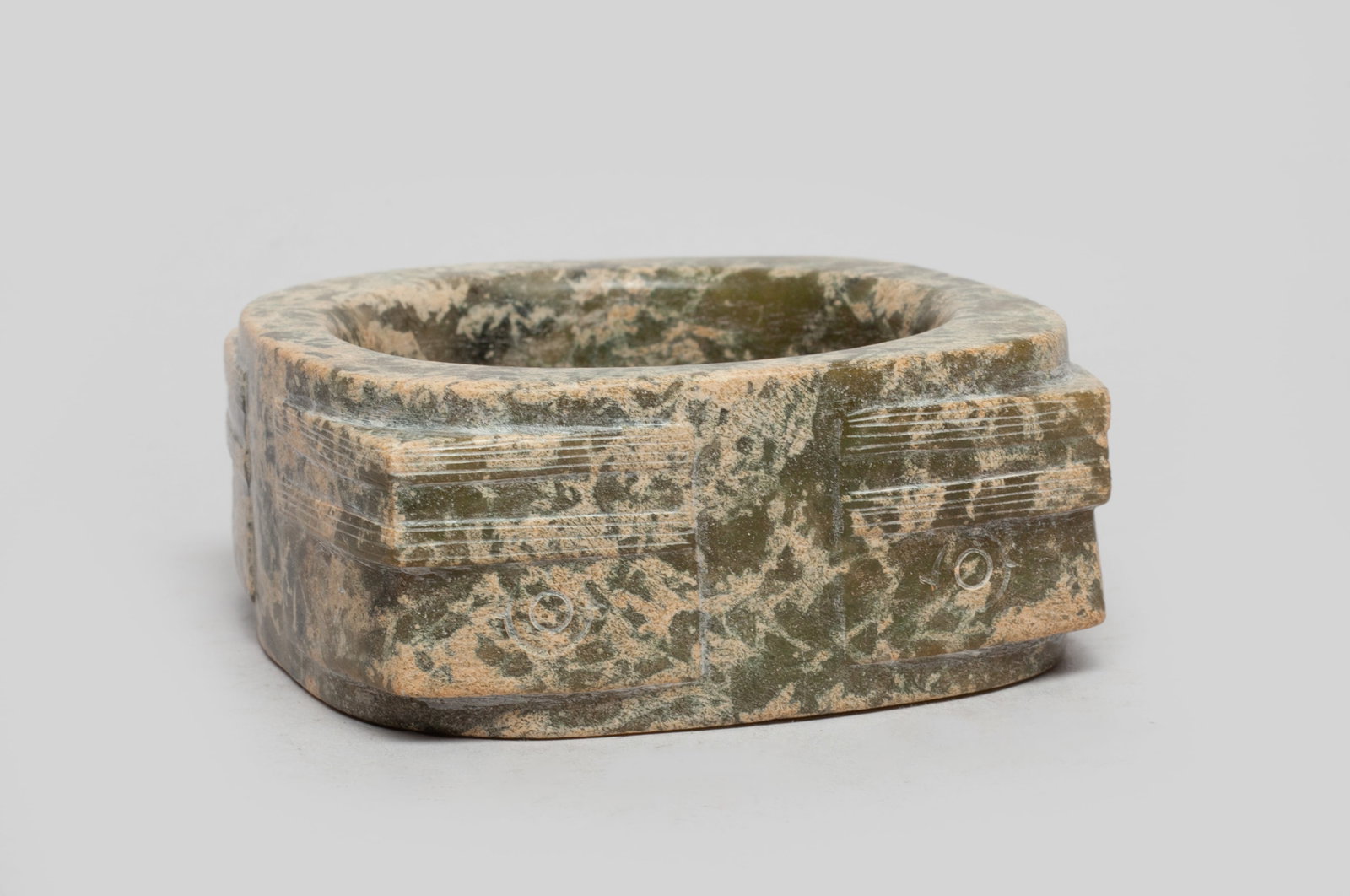 Chinese Russet Jade Sculpture of Cong: Carved with thick walls and of square form, the corners carved with taotie masks below incised parallel lines, the matrix of moss green colored tone and mottled with russet and buff inclusions. Approx