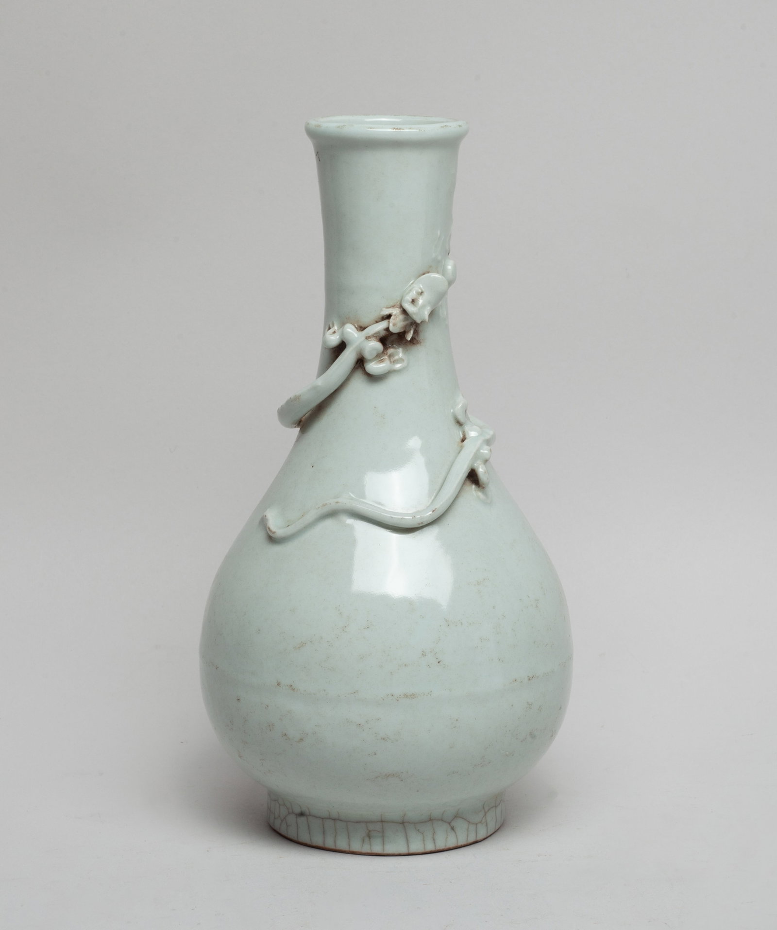 Chinese White Glazed Porcelain Dragon Vase: The pear-shaped body rising from a short foot to a tall slender neck, carved in raised relief with a sinuous dragon pursuing a flaming 'pearl', covered all save for the foot in mottled grayish white g