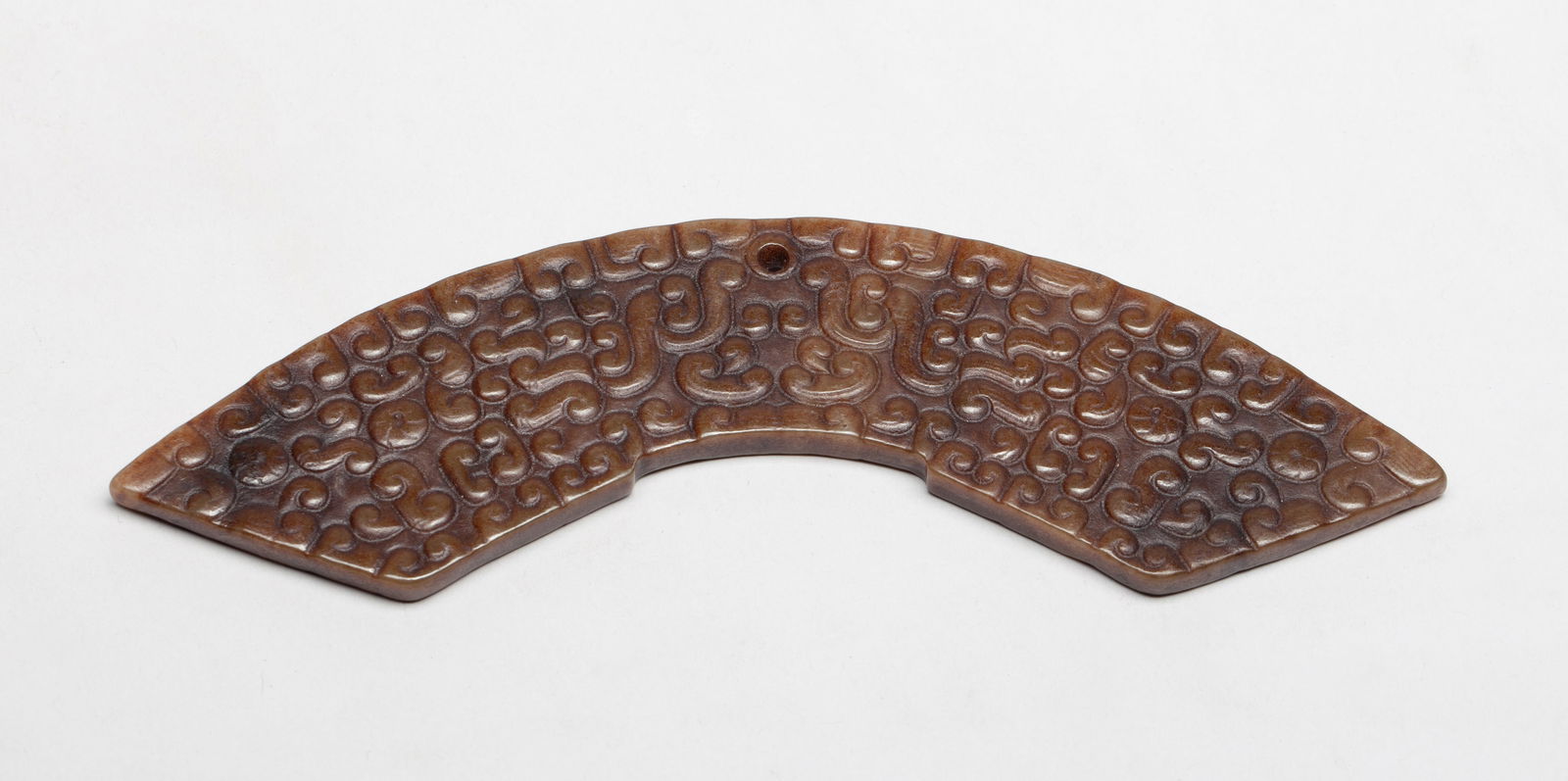 Estate Chinese Jade/ Stone Carved Pendant: Of arc shape, carved on both sides with dense archaic scrolls, drilled at the central top for suspension. Approx. 5.8*1.3 inch.