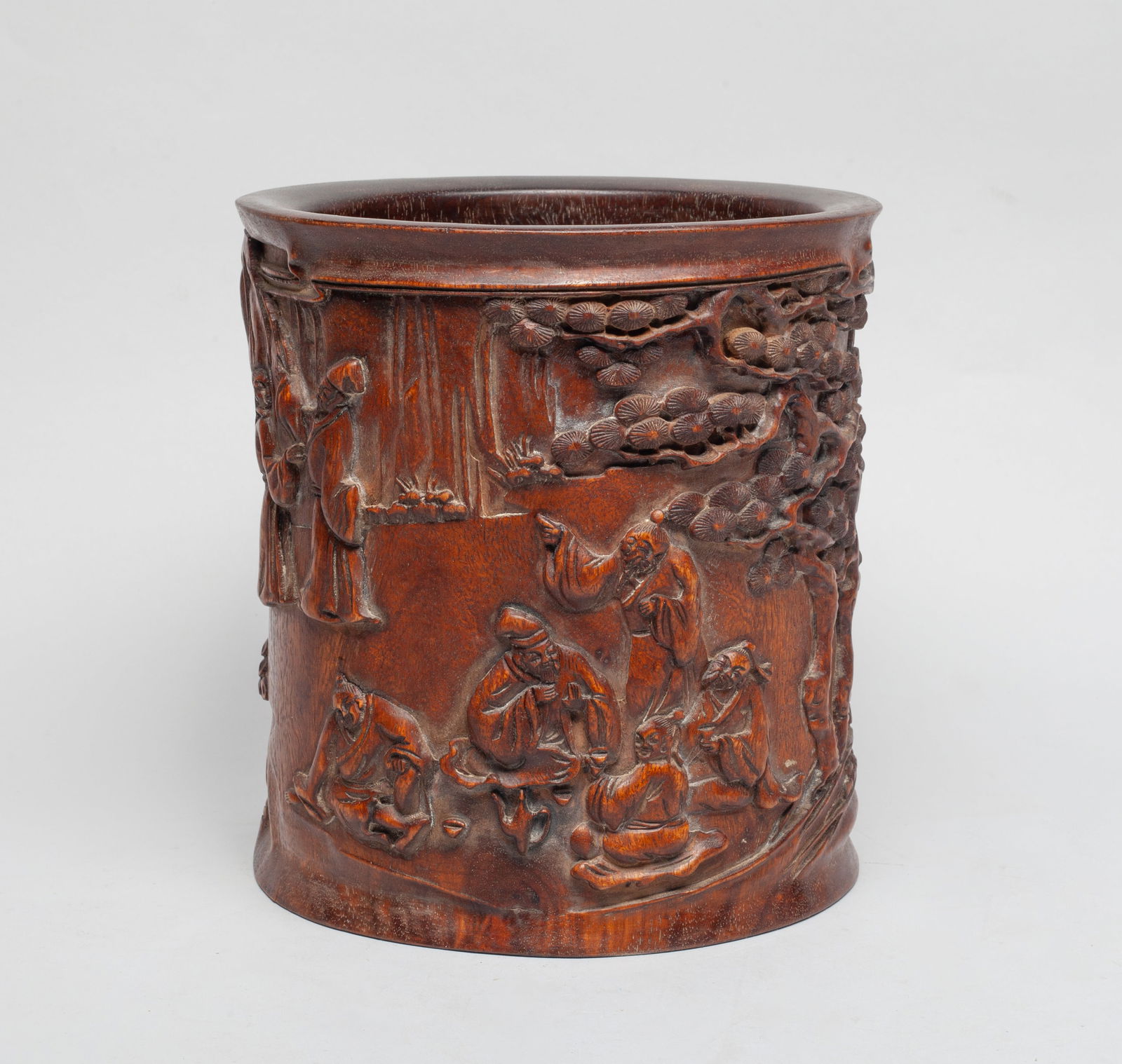 Large Chinese Carved Wood Brush Pot: Of cylindrical form, the exterior carved in deep relief with a continuous scene of figures amongst pine trees, a mountainous landscape in the distance, the bottom pierced with an aperture and set with