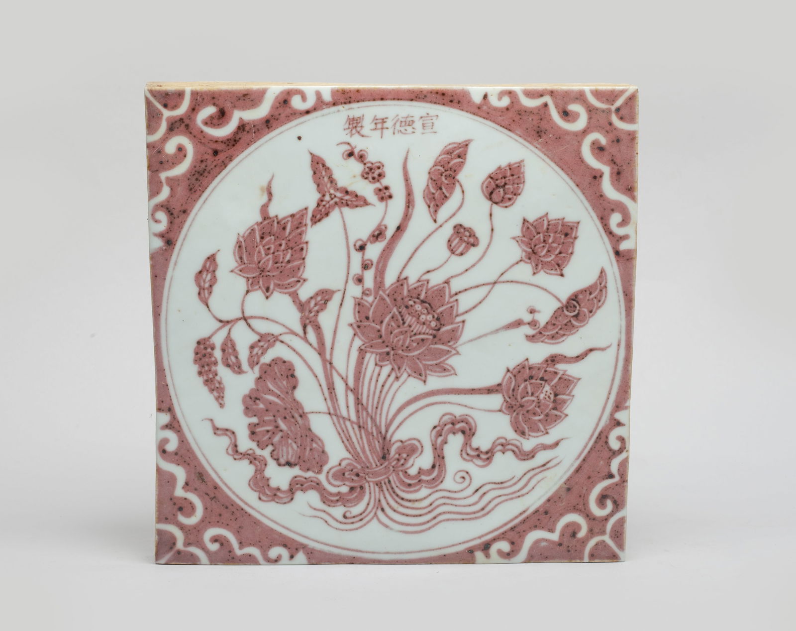 Collectible Chinese Copper Red Porcelain Tail: Of square shape, painted in copper red with a circular panel of beribboned lotus, marked with four characters. Approx. 7.7*7.7*1 inch.
