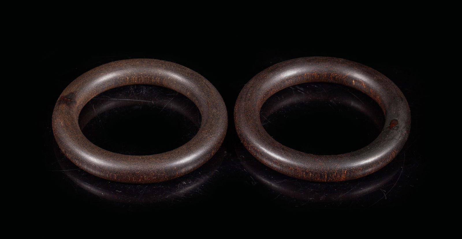 Two Chinese Agarwood Bangles: Two Chinese agarwood carved bangles. Approx. 3.35 inch outer diameter, 2.35 inch inner diameter (larger bangle), 65 gram (total weight). The Estate of the Stone Closed Sale, Pasadena, 2004.