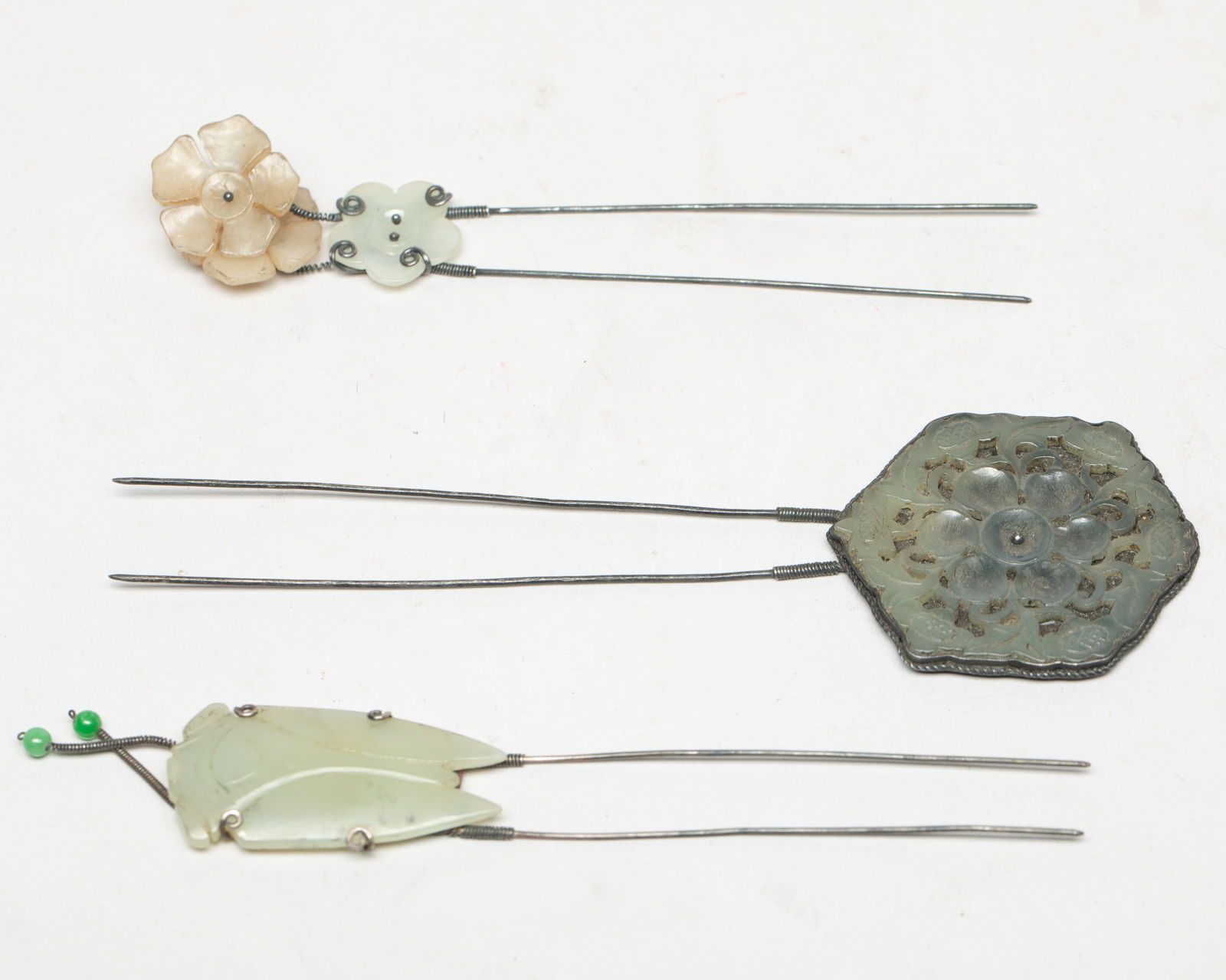 Set Chinese Jade, Silver Hair Pins: Set of three Chinese jade and silver hairpins, one carved with three plum blossoms, one with a cicada, the other with hexagonal plaque reticulated with a band of flowers surrounding a central bloom. A