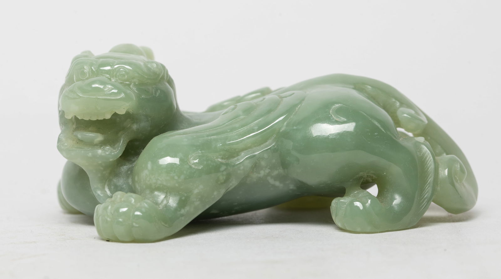 Rare Chinese Celadon Jade Beast Sculpture: The mythical beast powerfully and compactly carved with its head turned to the left, the flattened head crowned with a single horn, the jaws open to reveal the menacing teeth, the front right leg exte