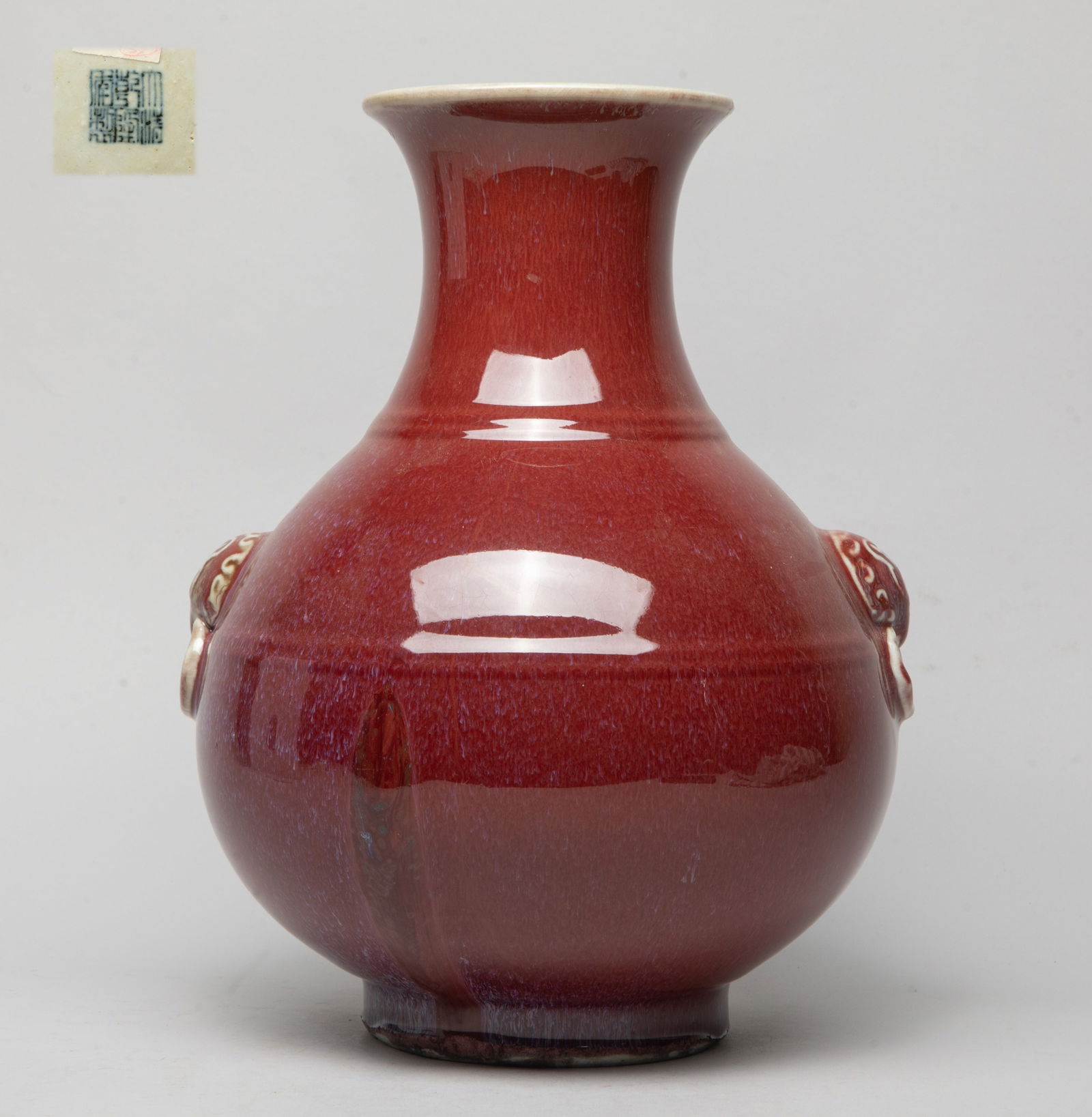 Large Chinese Export Porcelain Vase: The globular body rising from a short foot to a waisted neck and a flared rim, molded with a pair of faux-ring masks handles, the exterior and interior neck covered in red glaze with milky blue streak