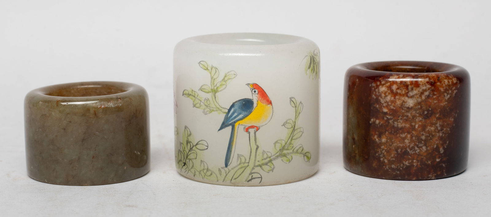 Chinese Jade, Peiking Glass Thumb Rings: Including two Chinese jade carved thumb rings, the surface finely smoothed and polished, and a white Peiking glass thumb ring, painted with bird, bamboo and flower, marked with four characters. Approx