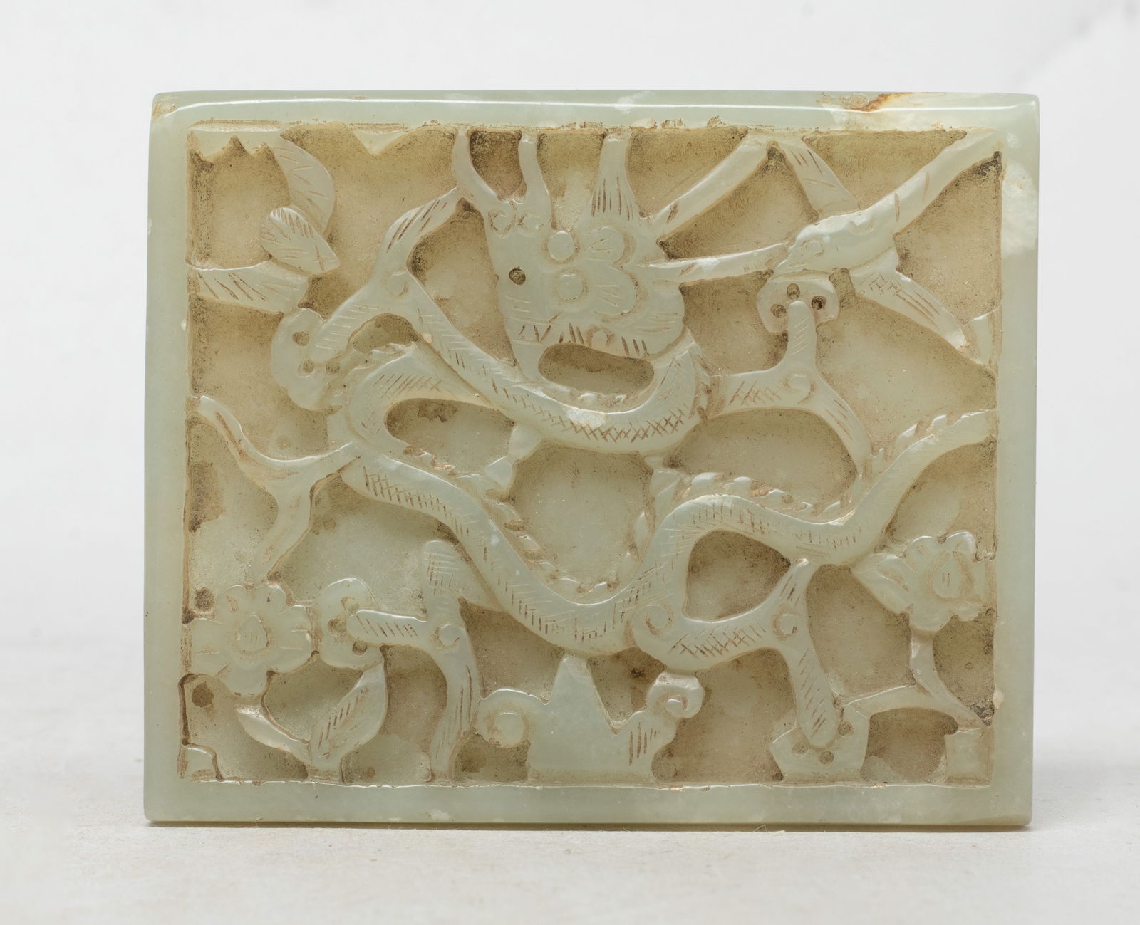 Estate Chinese Large Jade Dragon Plaque: Of rectangular shape, carved with a bat, a bird, a sinuous dragon, and flowers, the stone of pale celadon tone with faint russet inclusions. Approx. 3.23*2.66 inch.