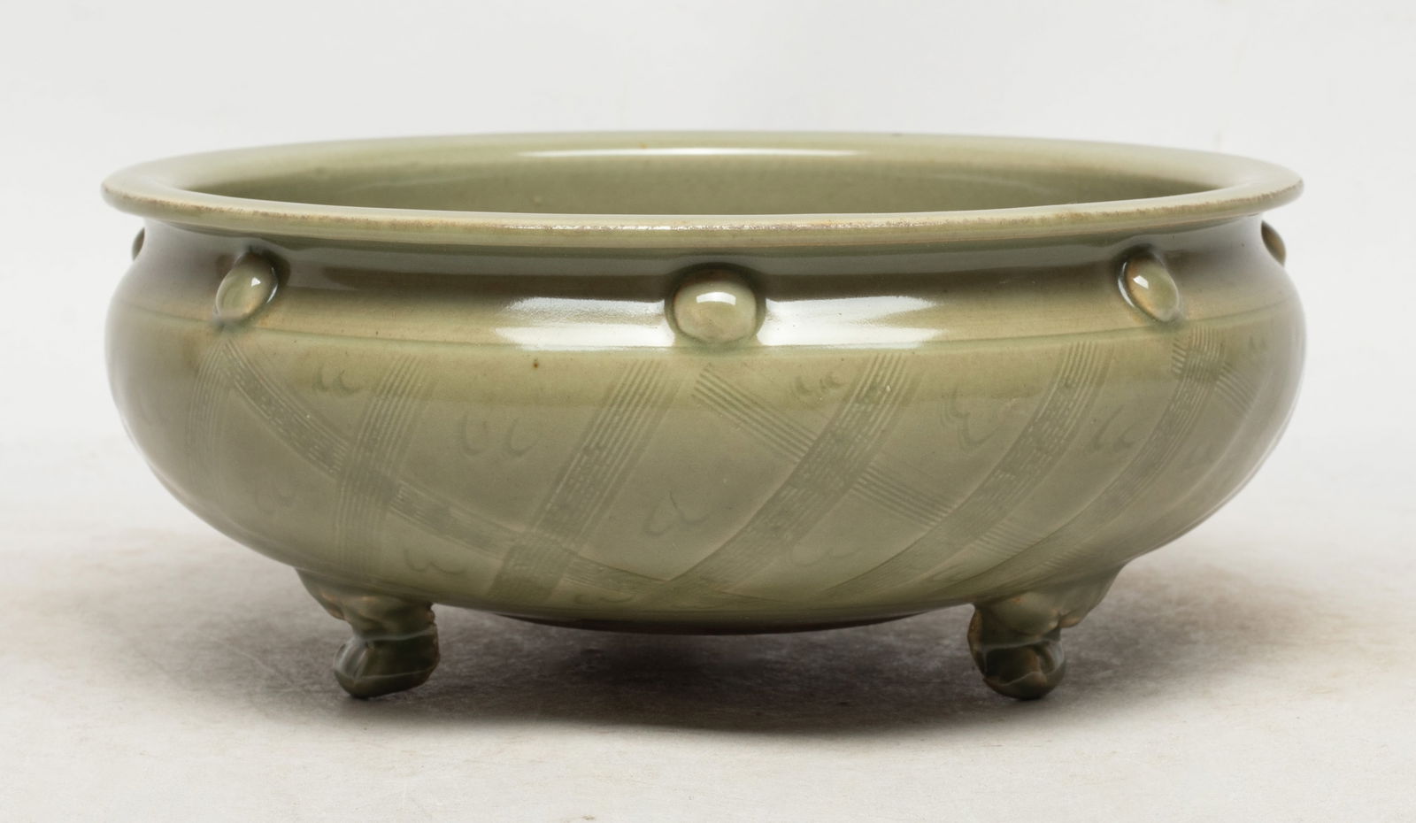 Large Chinese Longquan Porcelain Censer: Of compressed ovoid form, with three short spreading mask form legs, the exterior incised with checked motif, overall covered with celadon glaze. Approx. 7.6*3.1 inch.