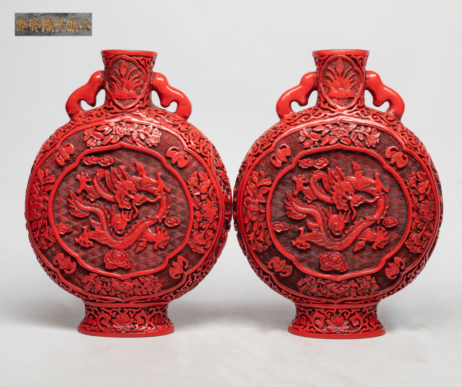 Two Chinese Export Cinnabar Vases: Each vase carved with a sinuous dragon pursuing a flaming pearl on either side, the flanks with medallions of bogu pattern, ground with lotus foliage, the bottom marked with six characters. Approx. 10