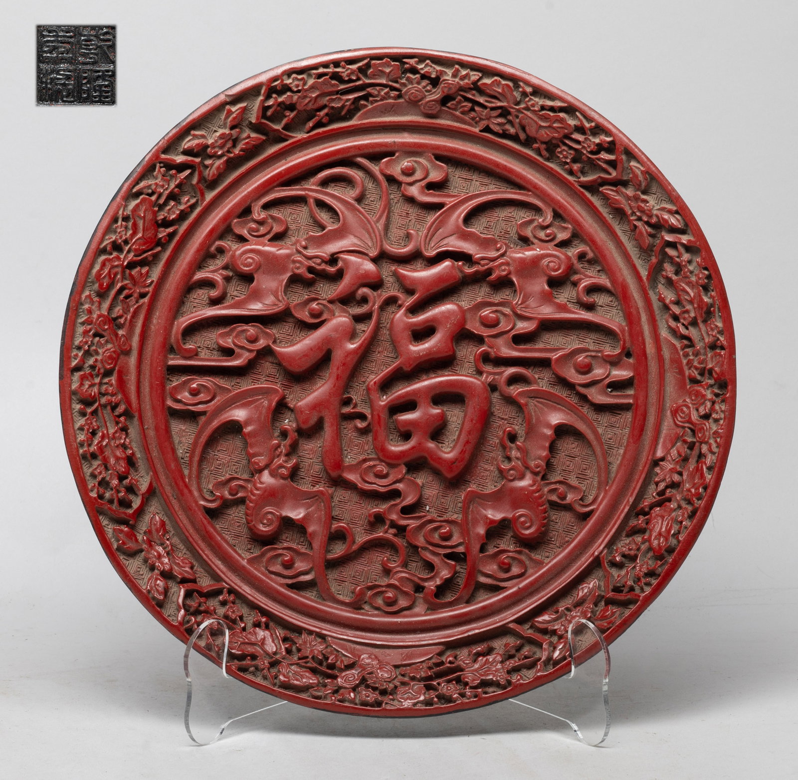 Chinese Export Cinnabar Plate: The interior centre carved in high relief with a Fu character and four bats amidst clouds, the sides with blossoming flower branches, the bottom inscribed with a seal mark. Approx. 11.1 inch D.
