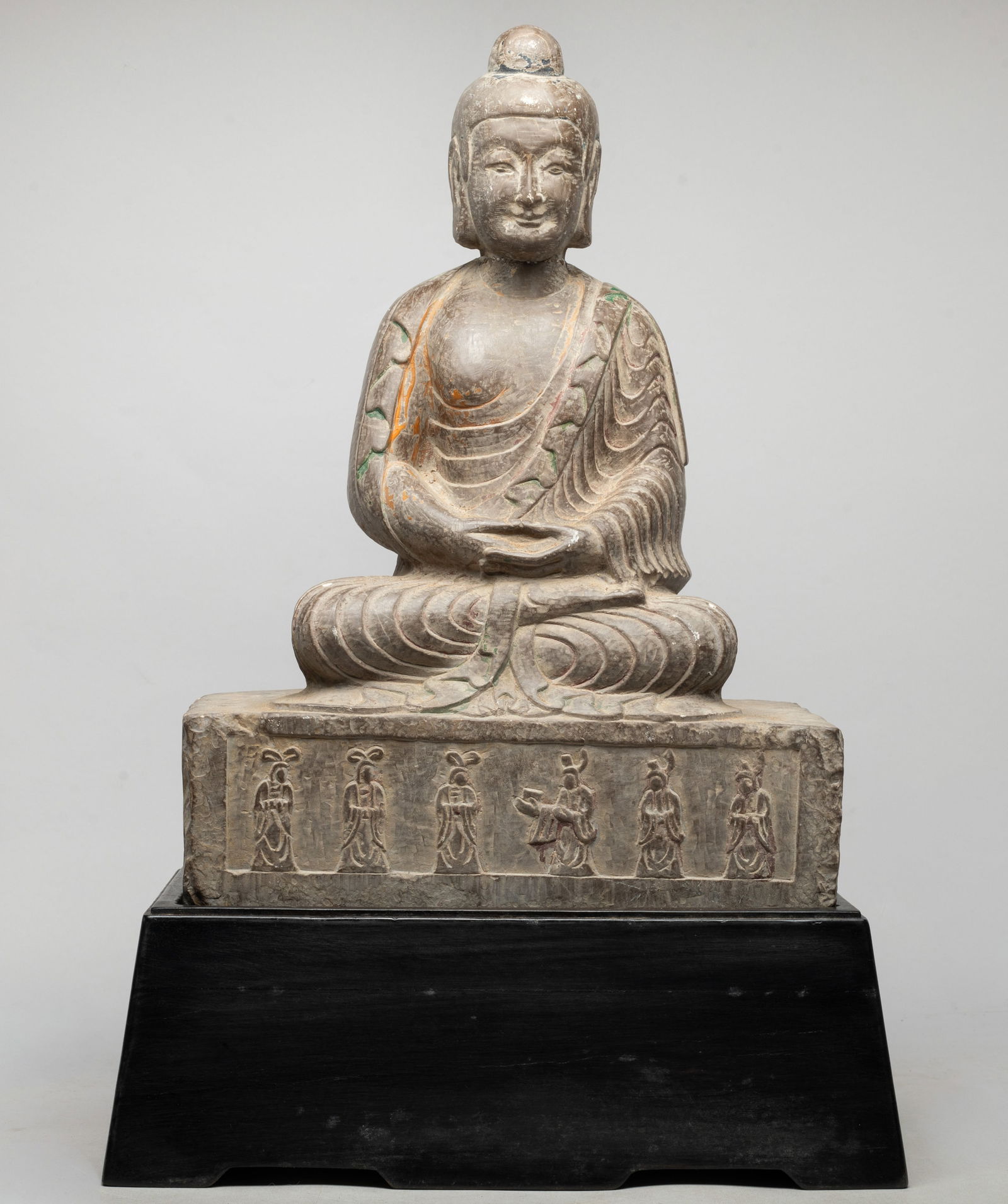 Large Chinese Stone Sculpture of Buddha: The Stone Buddha carved seated on a rectangular plinth detailed with six figures, the hands in dhyana mudra, wearing a loose-fitting robe, the face with serene expression, with a wood stand. Approx. 2