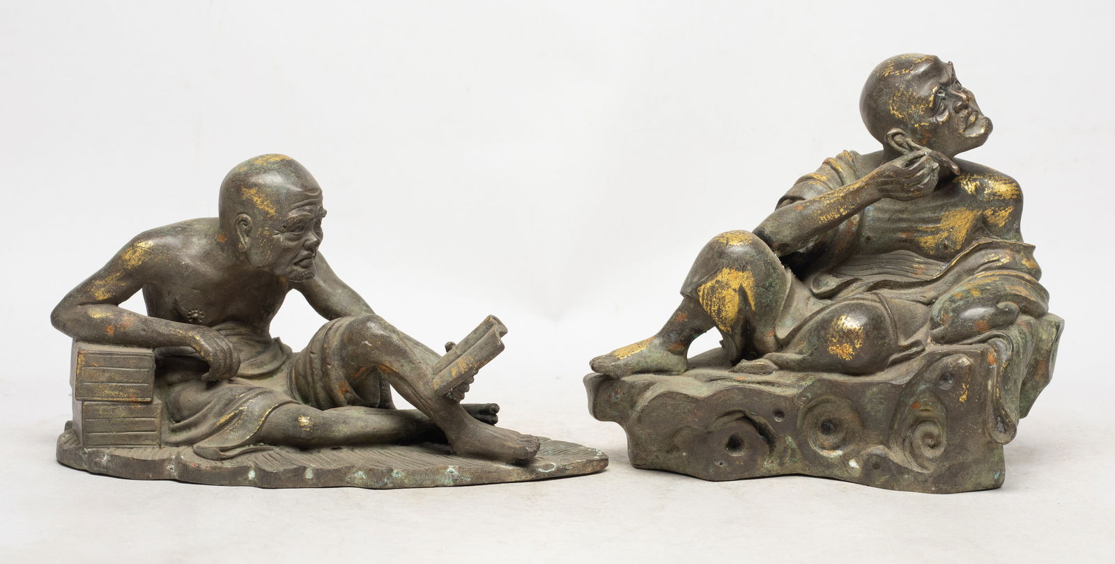 Two Chinese Bronze Sculptures of Luohan: Two bronze Luohan sculptures, one cast as Buddha sitting on a leaf reading book, the other cast as seated Luohan holding a twig in right hand. Approx. 8*4.4*4 inch (larger).