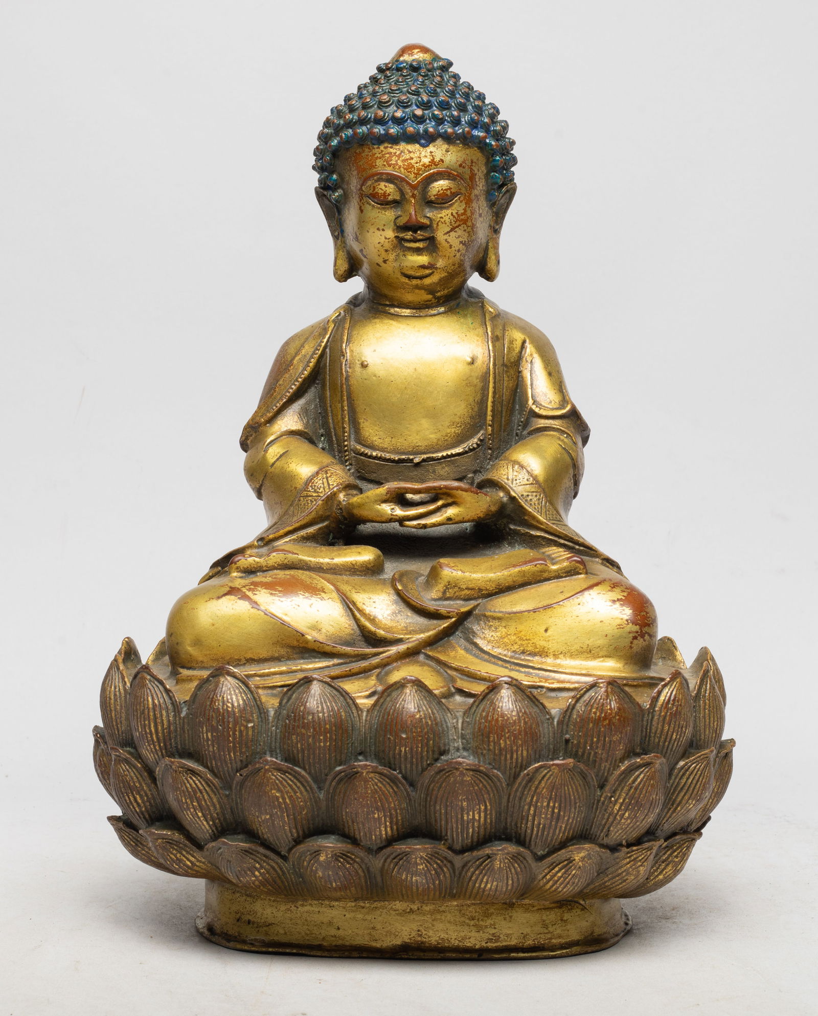 Chinese Gilt Bronze Sculpture of Buddha: With high ushnisha, full face, and pendulous earlobes, attired in the loose garments of a monk as he sits dhyanasana on a circular plinth formed as a lotus flower, the hands in dhyana mudra. Approx. 1
